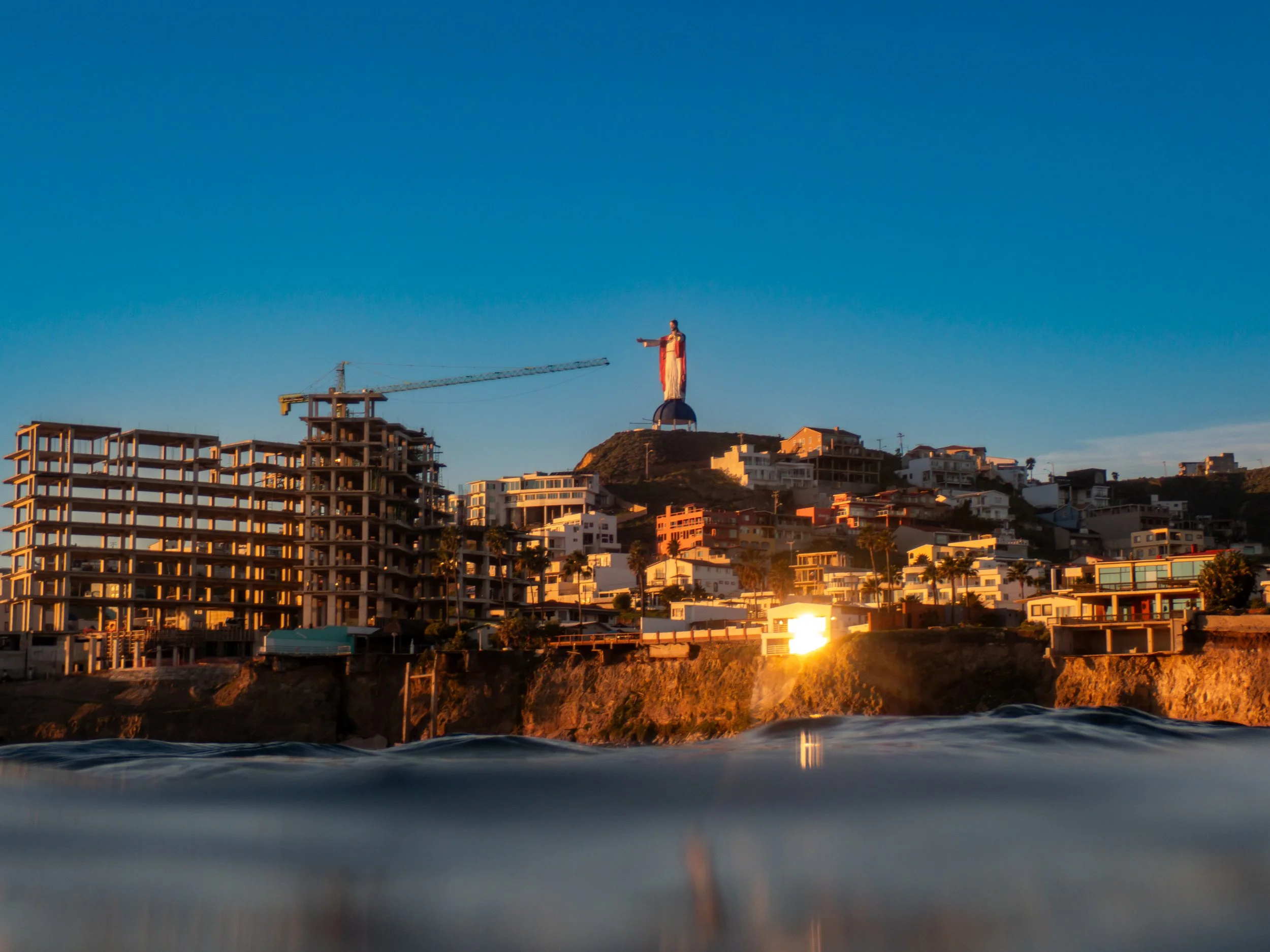 View of the city of San Francisco with the Christo Redentor statue on a hilltop, under a clear blue sky, with water in the foreground.