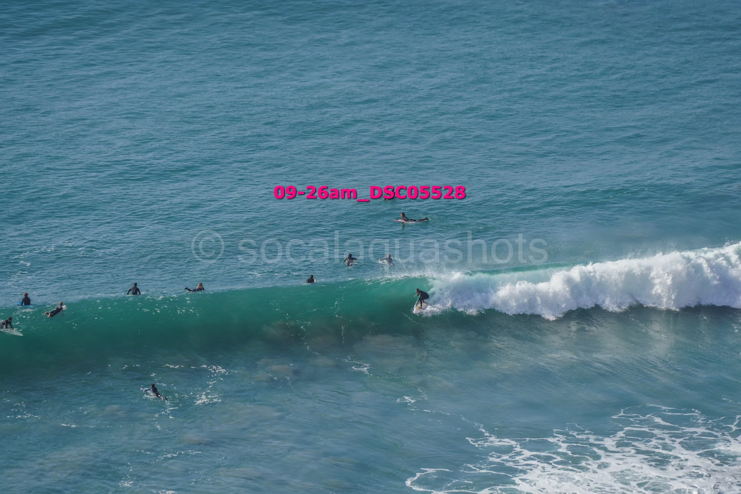 Several surfers in wetsuits riding and waiting for waves in the ocean on a clear day.