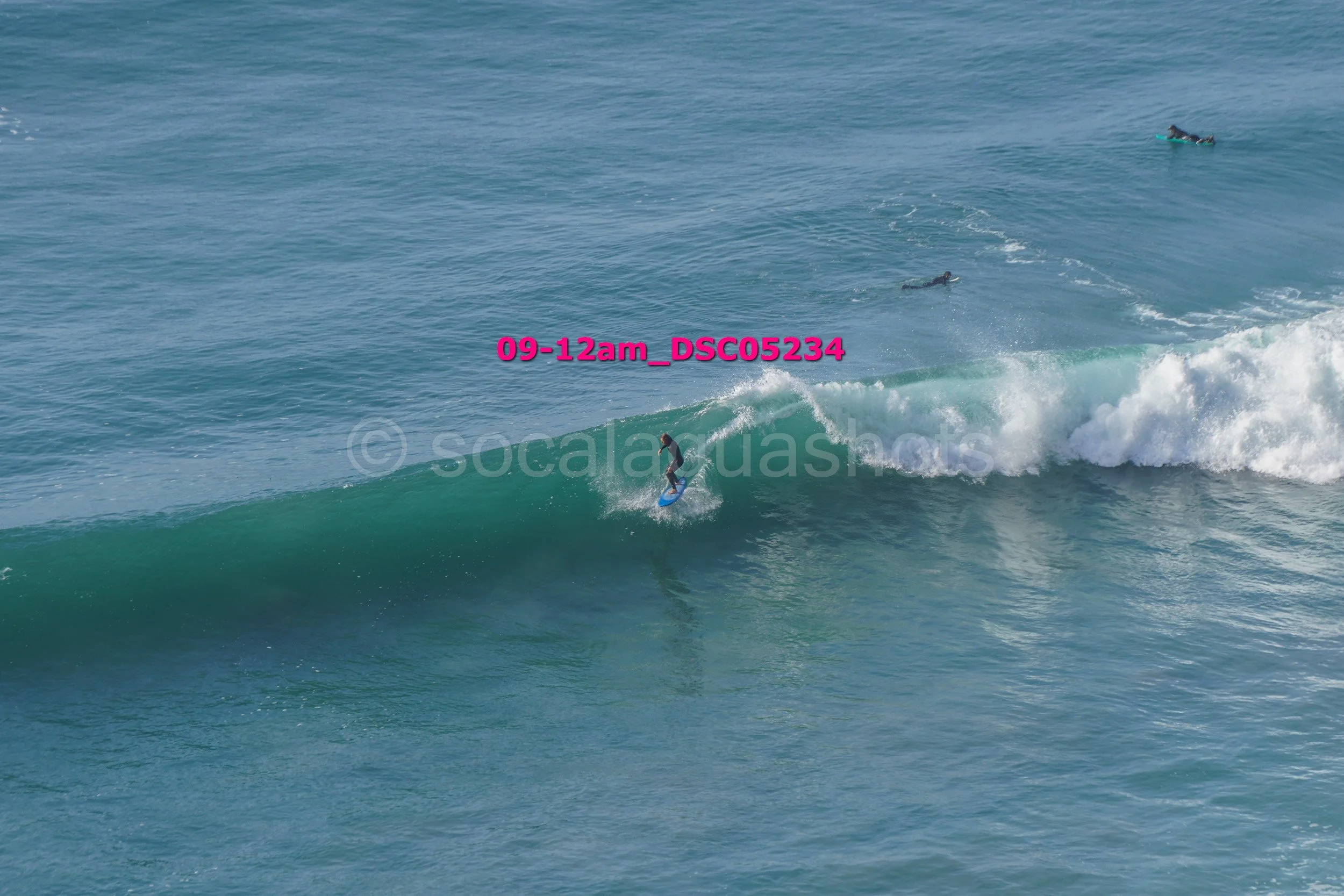 A person surfing on a wave in the ocean with a few other surfers in the background.