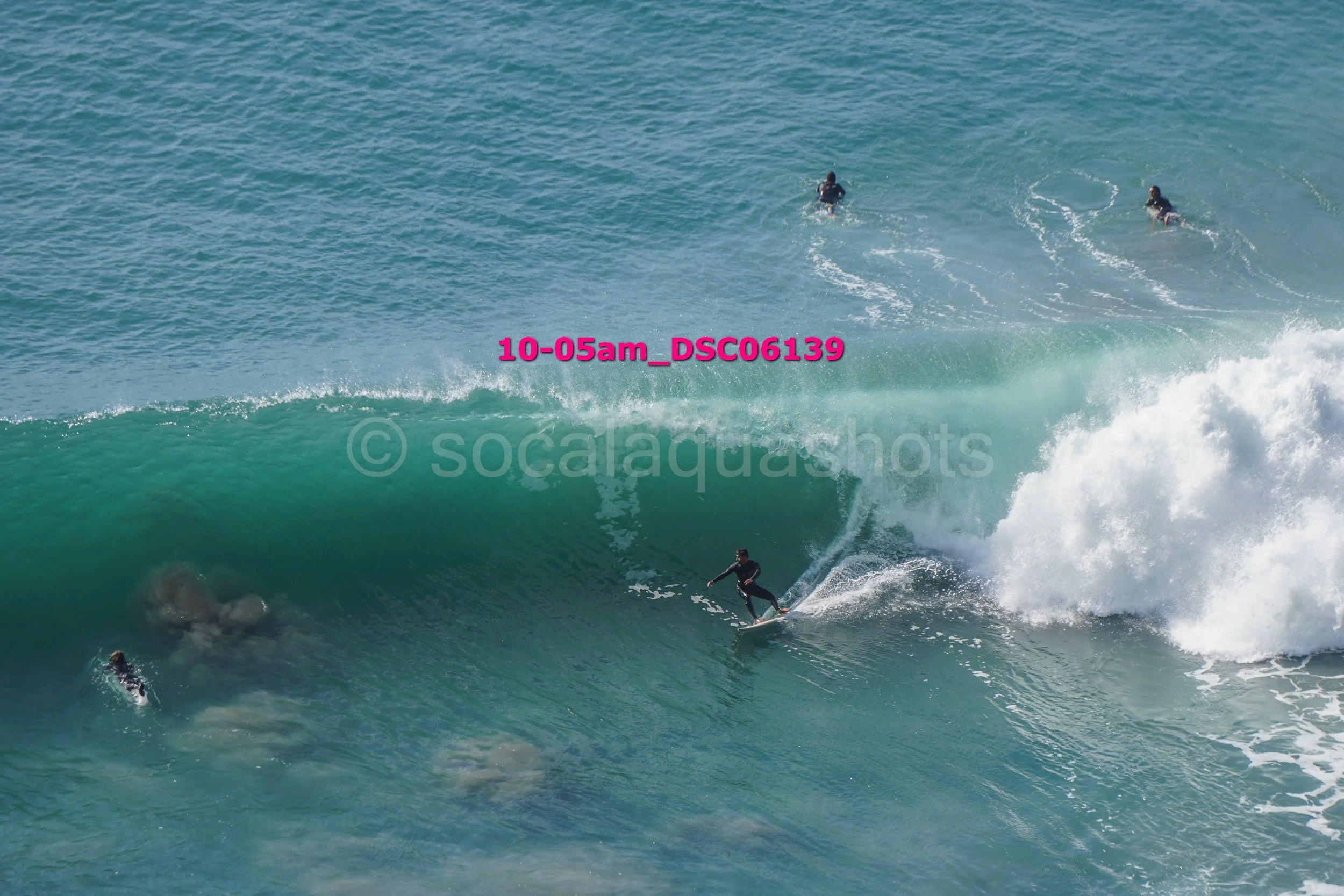 Surfer riding inside a large wave with several other surfers in the water nearby.
