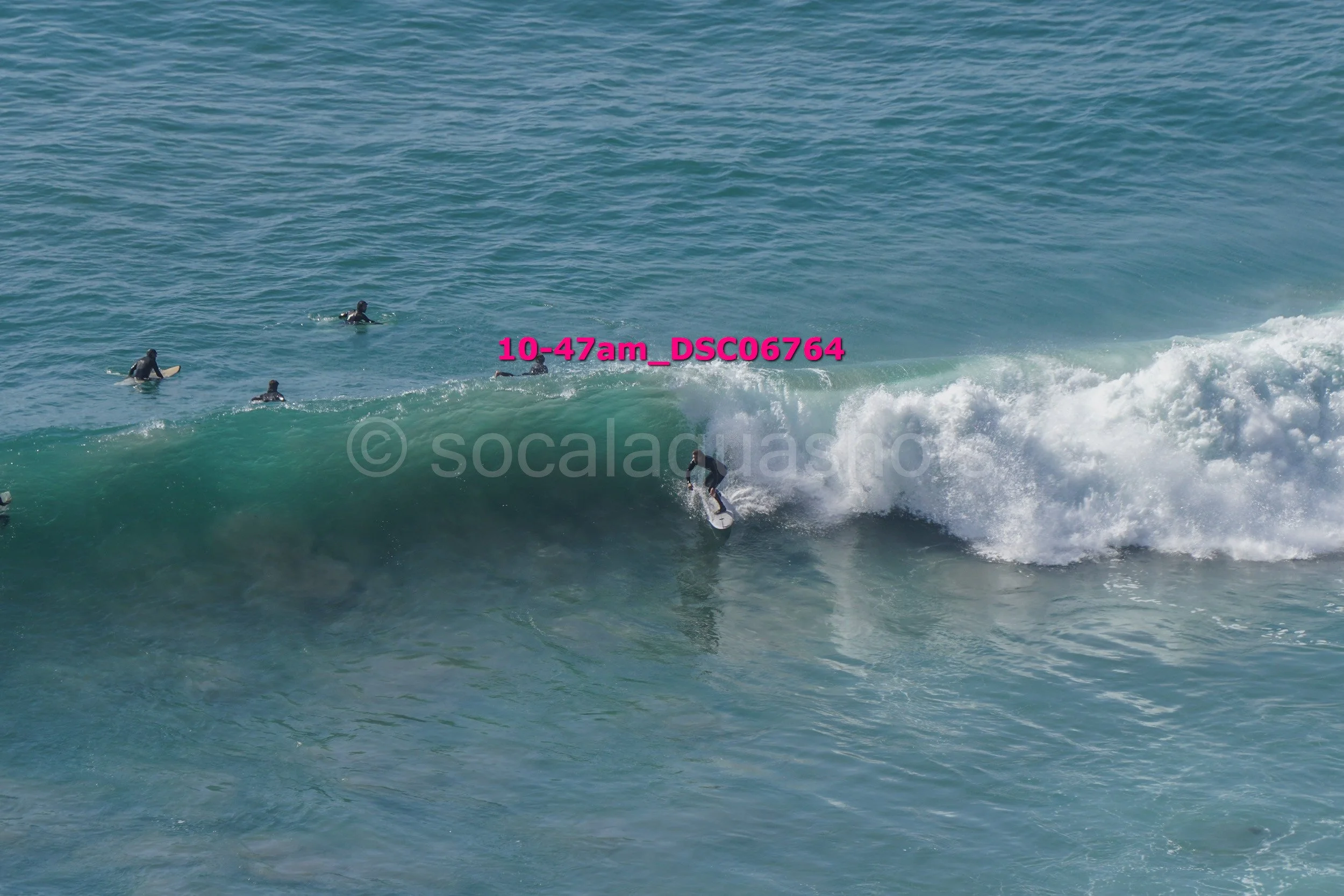Surfer riding a wave with several surfers waiting in the water nearby.