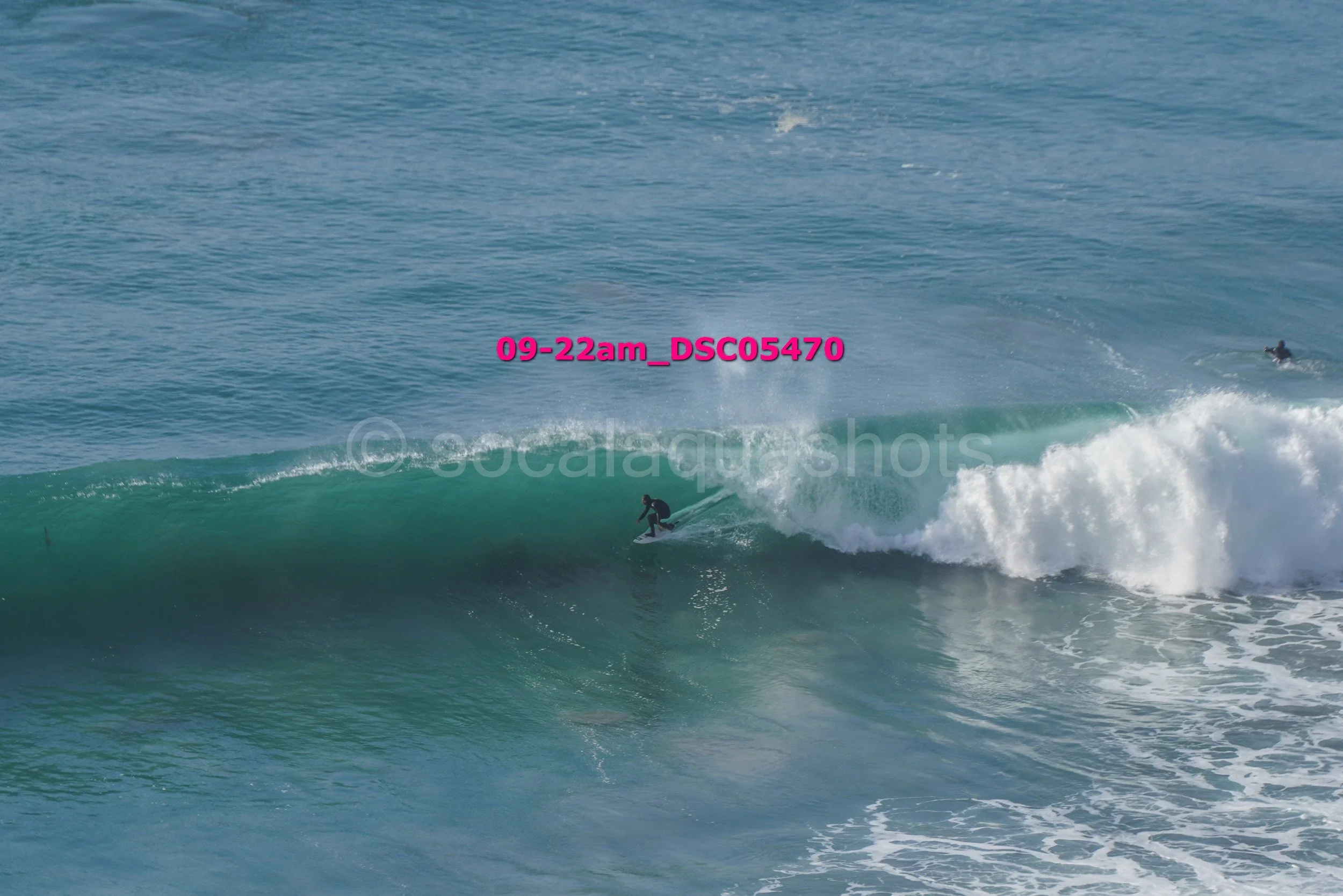 A surfer riding a large wave in the ocean during daytime with another surfer visible in the distance.