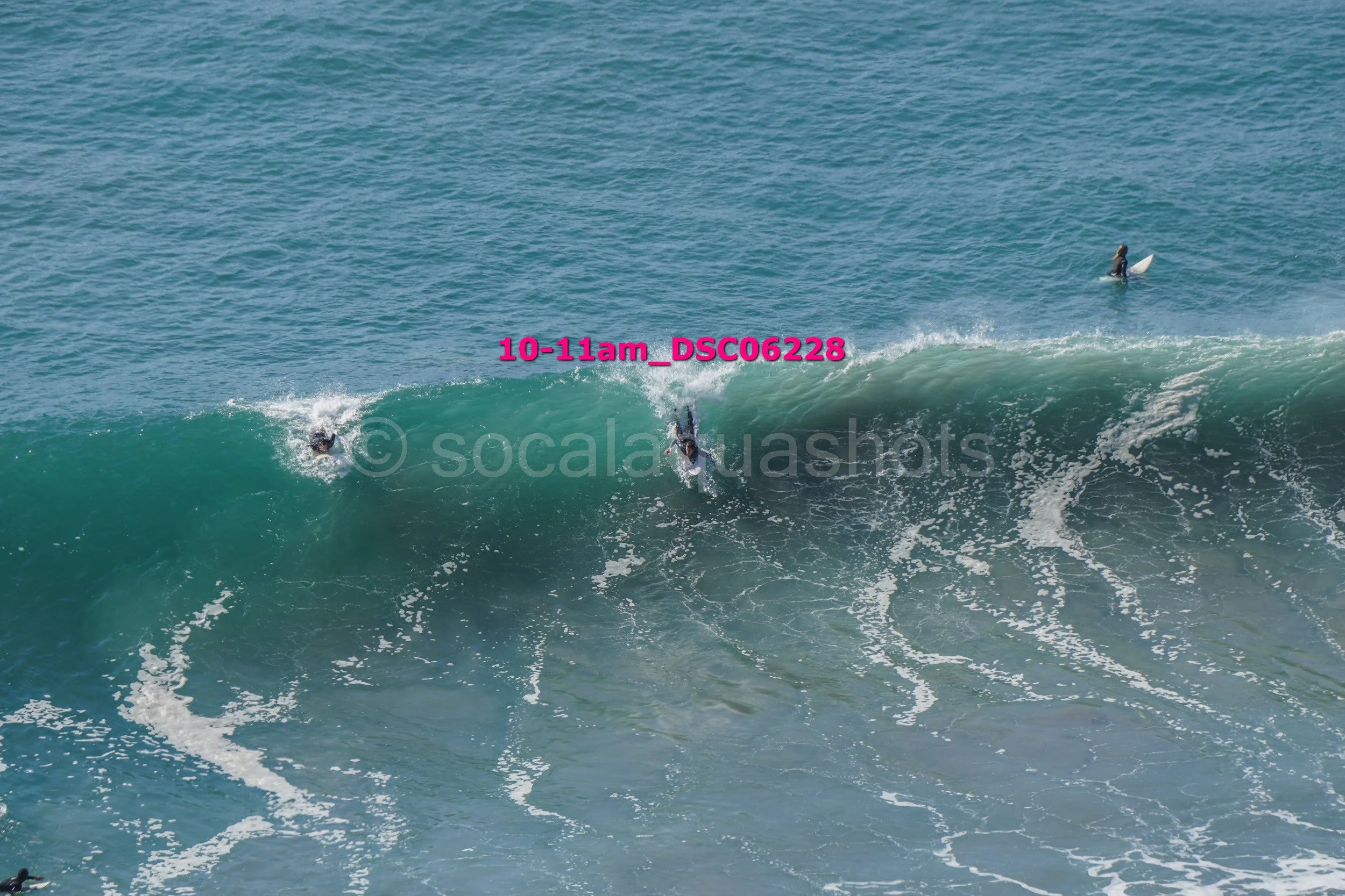 Two surfers riding a large wave in the ocean, with a boat in the distance, under a clear sky.