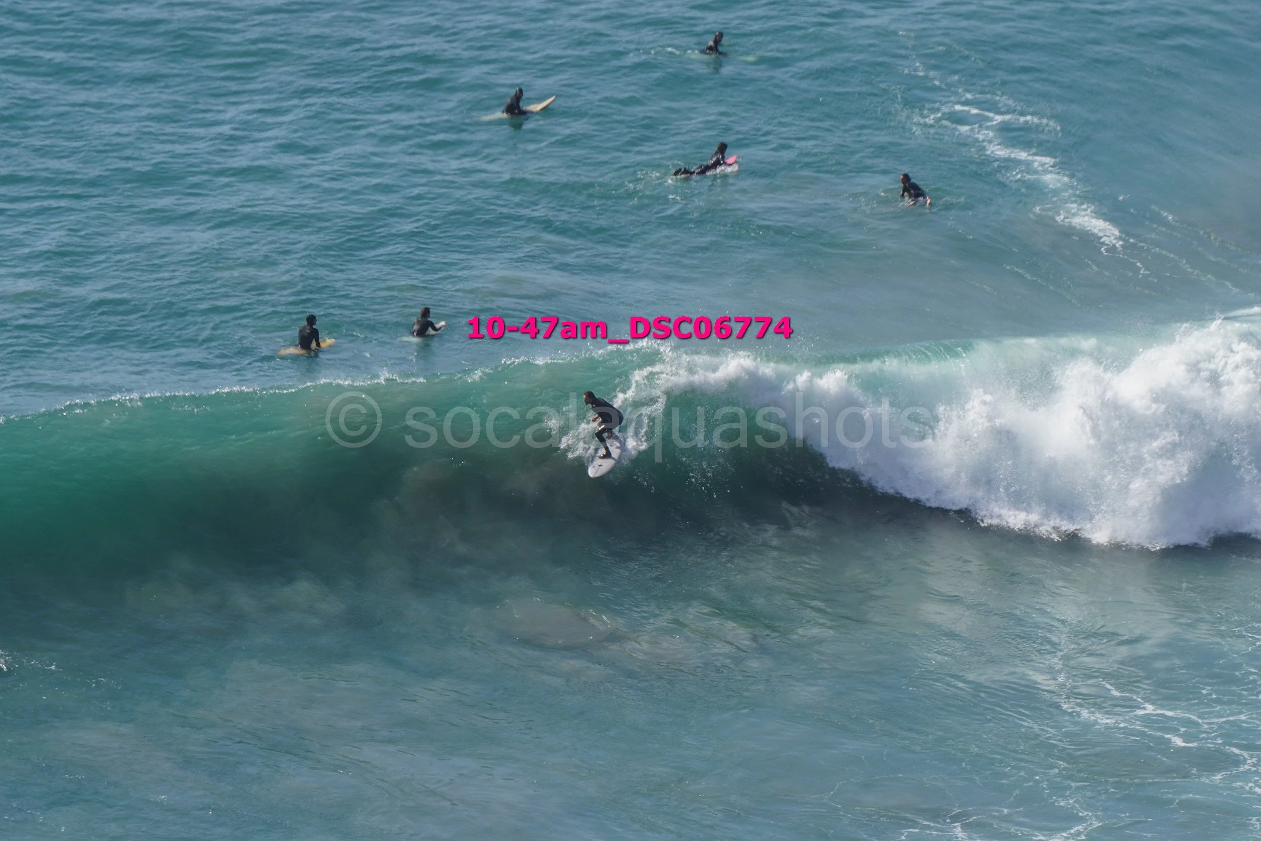 A surfer riding a wave while several other surfers wait in the water behind him.