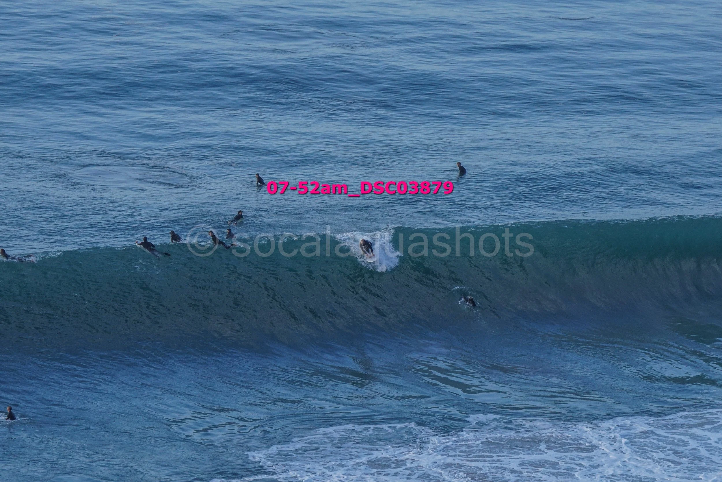 Multiple surfers in wetsuits surfing and floating in the ocean waves.
