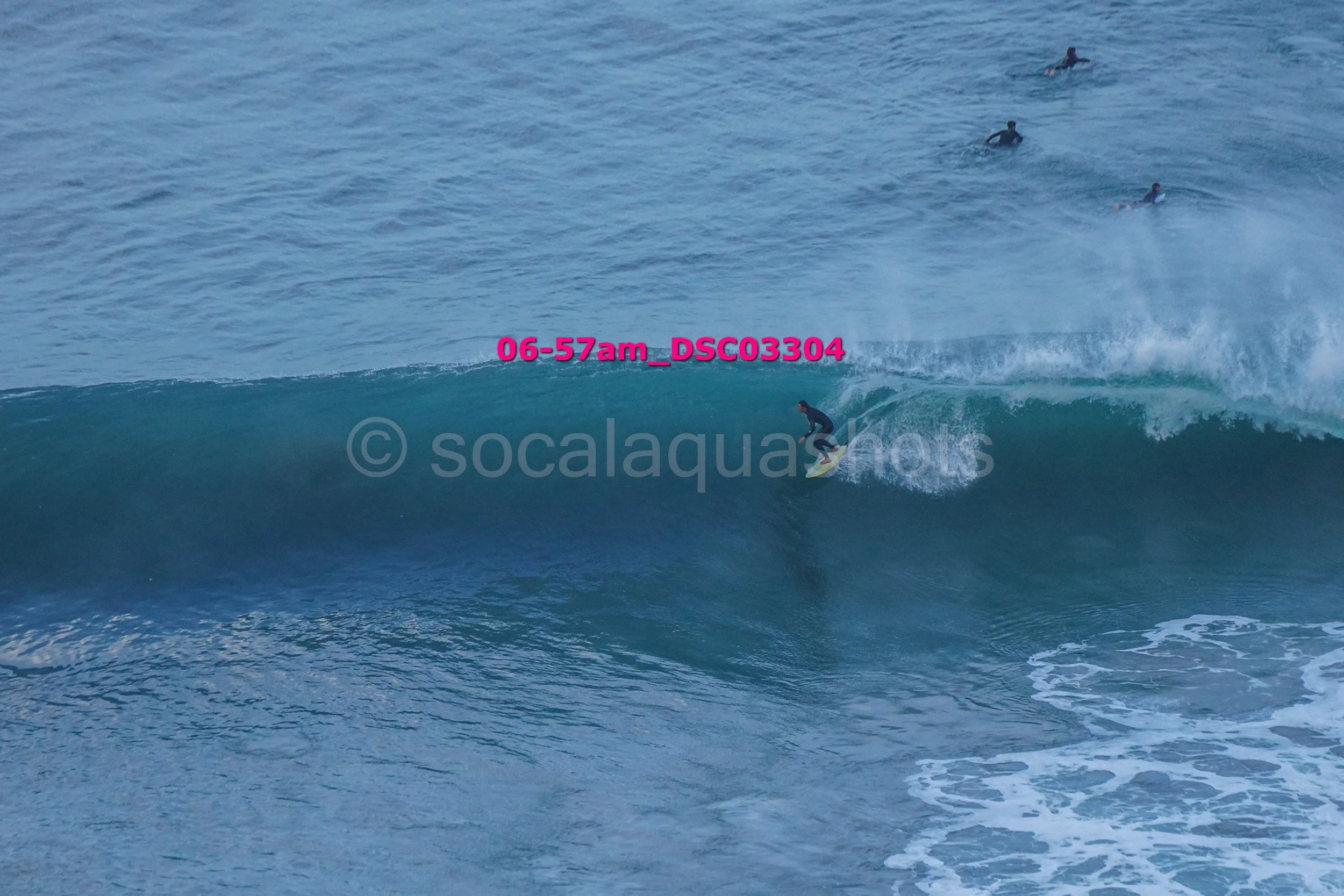 A person surfing on a large wave with several other surfers in the background in the ocean.