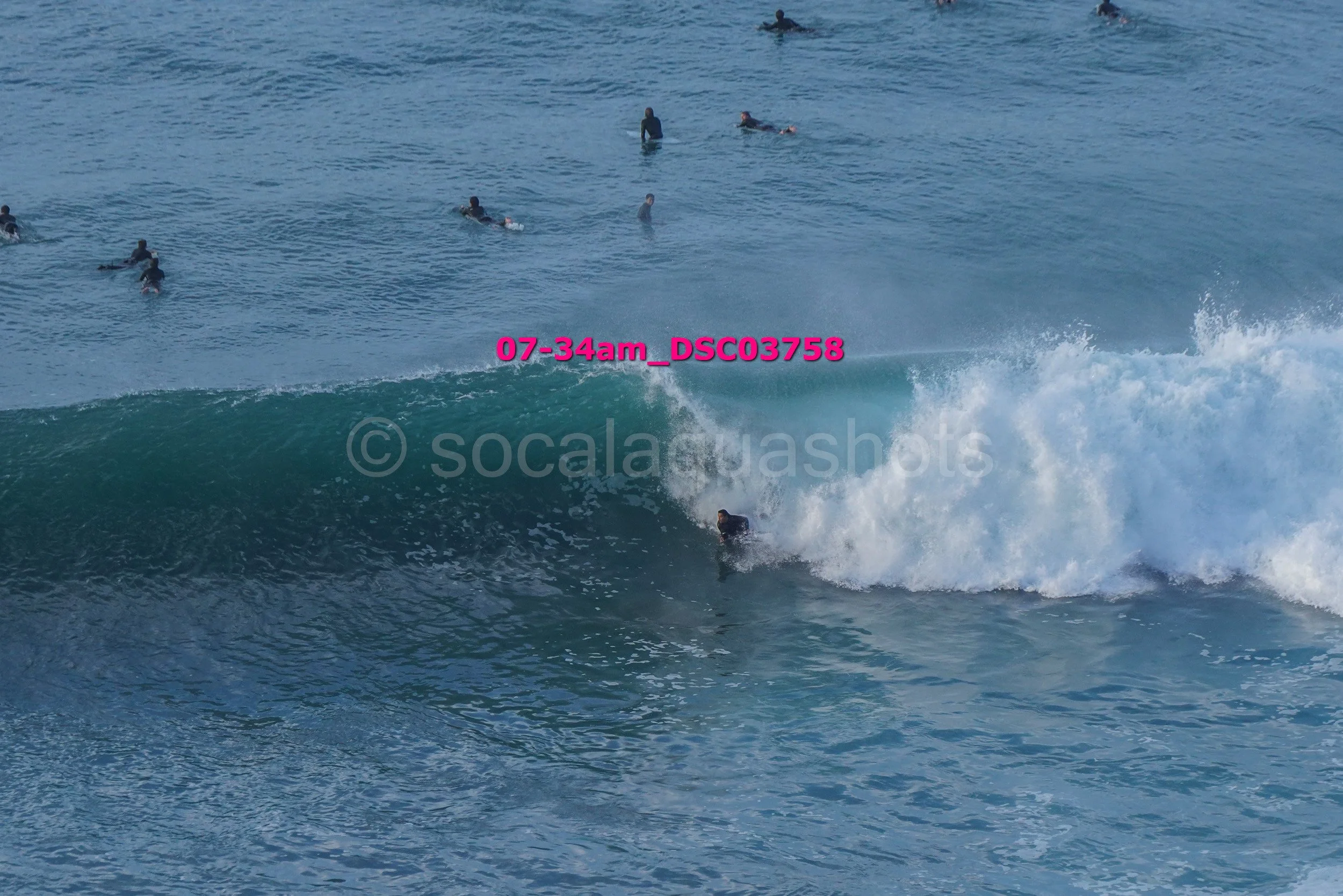 A surfer riding a wave with several people swimming in the water in the background.