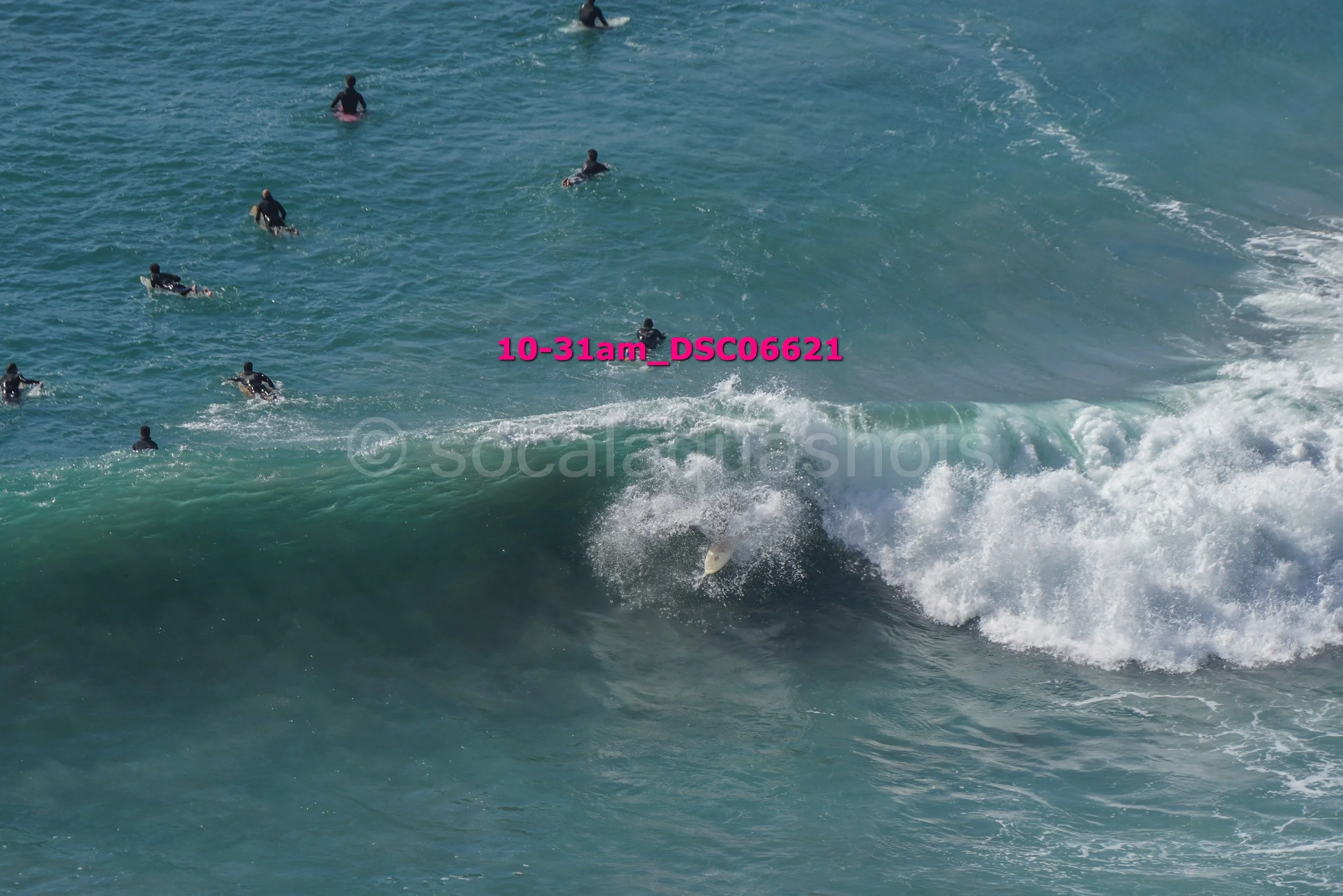 A surfer riding a wave in the ocean while other surfers and swimmers are in the water nearby.