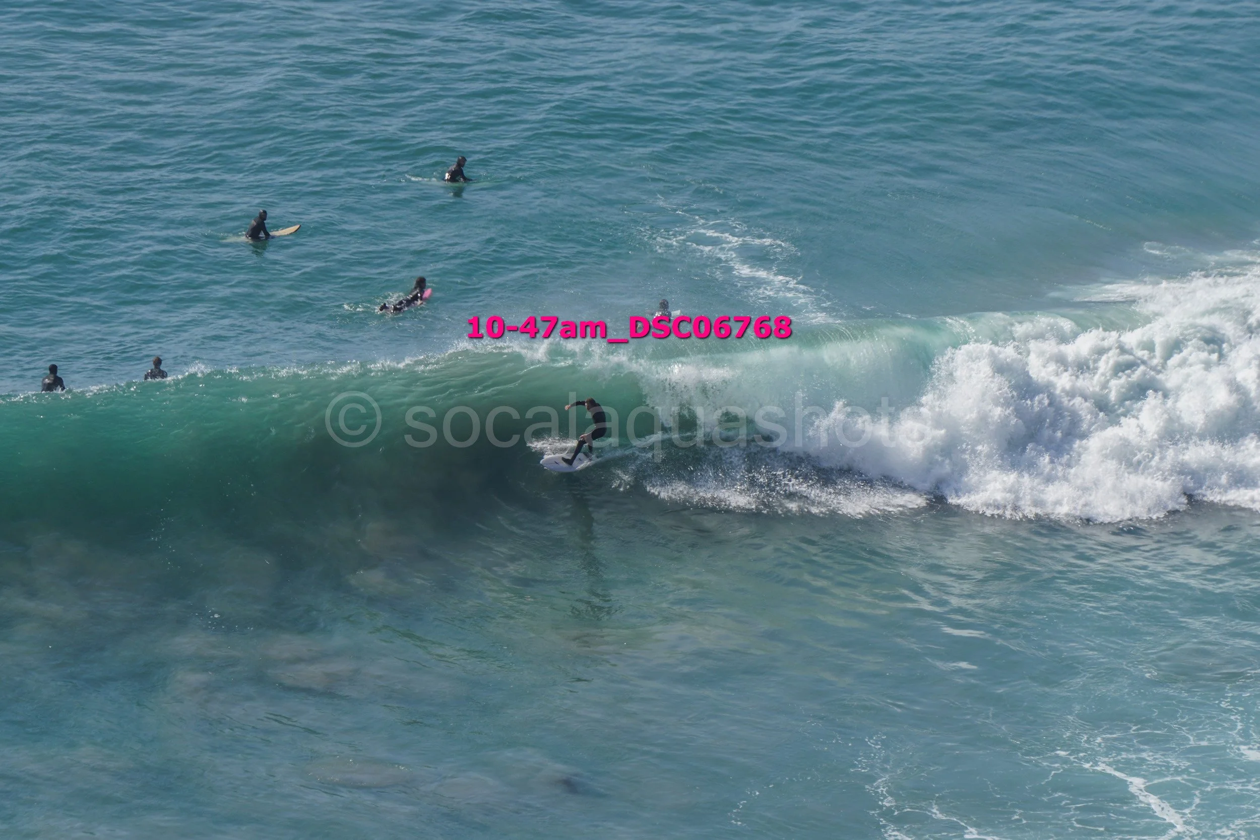Surfer riding a large wave with several surfers watching from the water in the background.