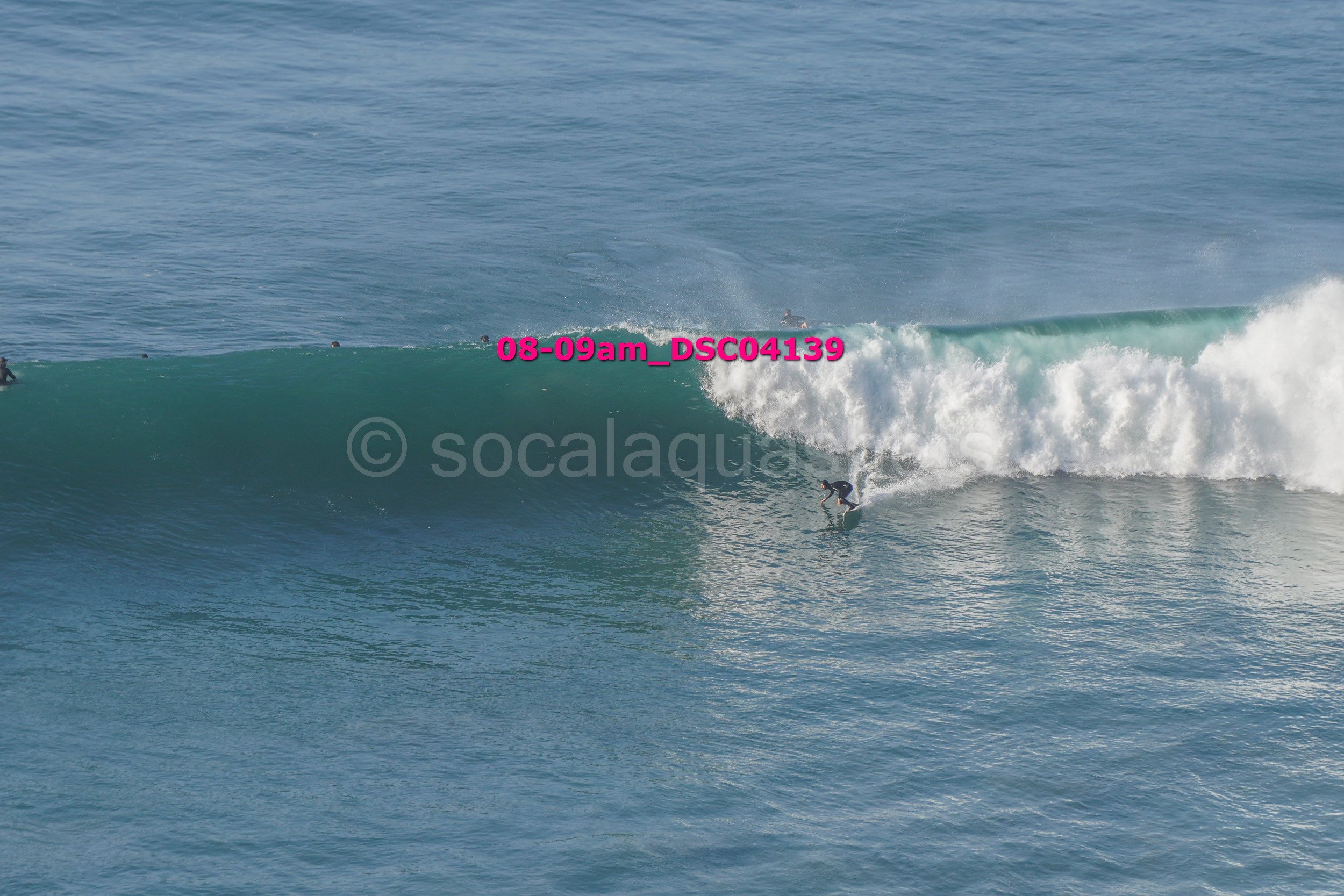 A surfer riding a large wave in the ocean with other surfers in the background.