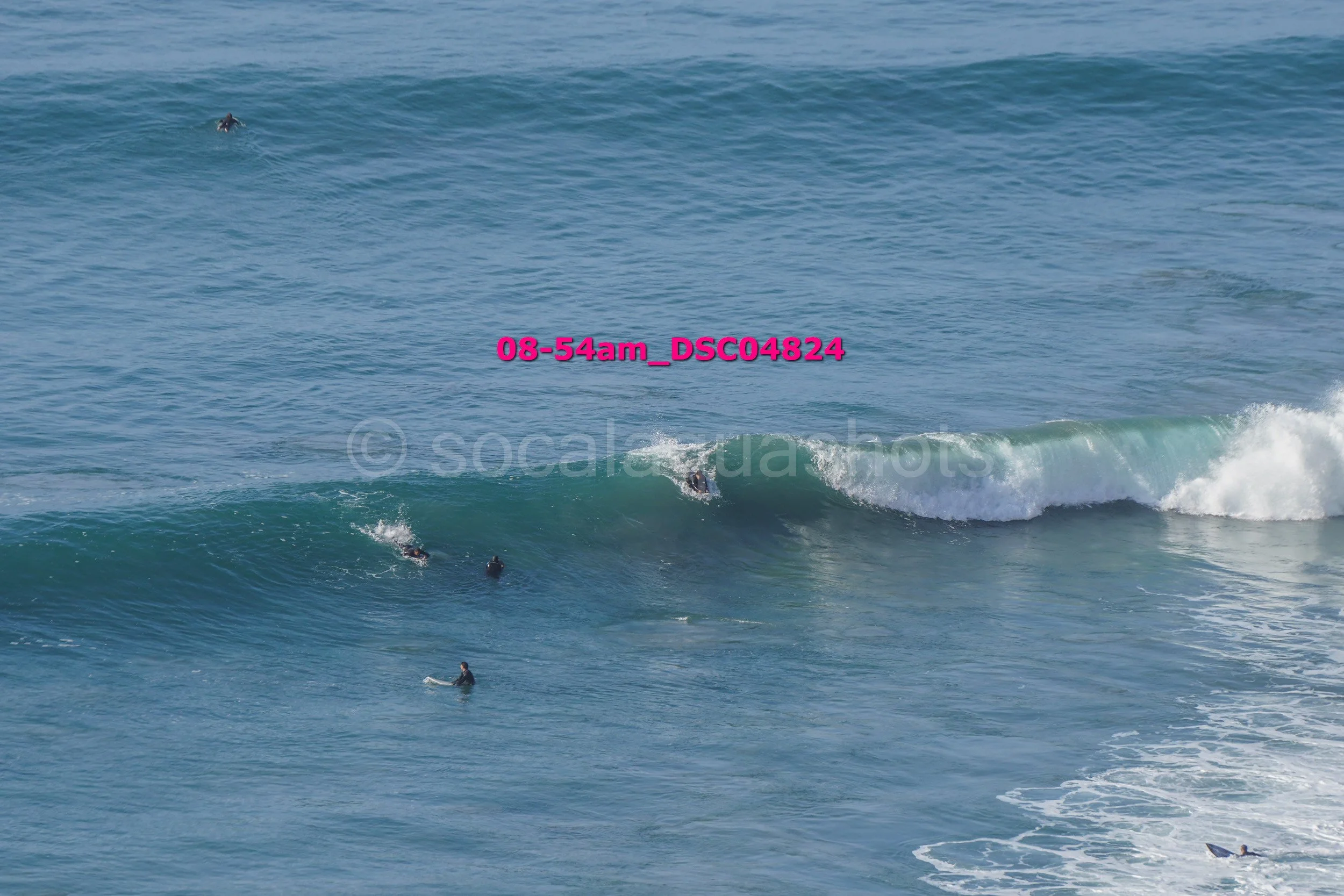 Several surfers in wetsuits are riding and waiting for waves in the ocean during daytime.