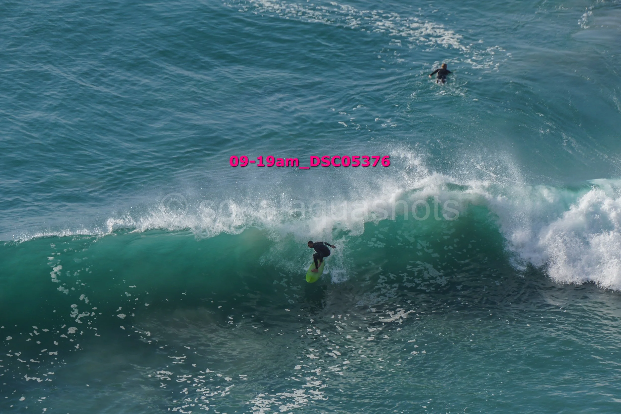 A person surfing on a wave in the ocean with another swimmer floating nearby in the water.