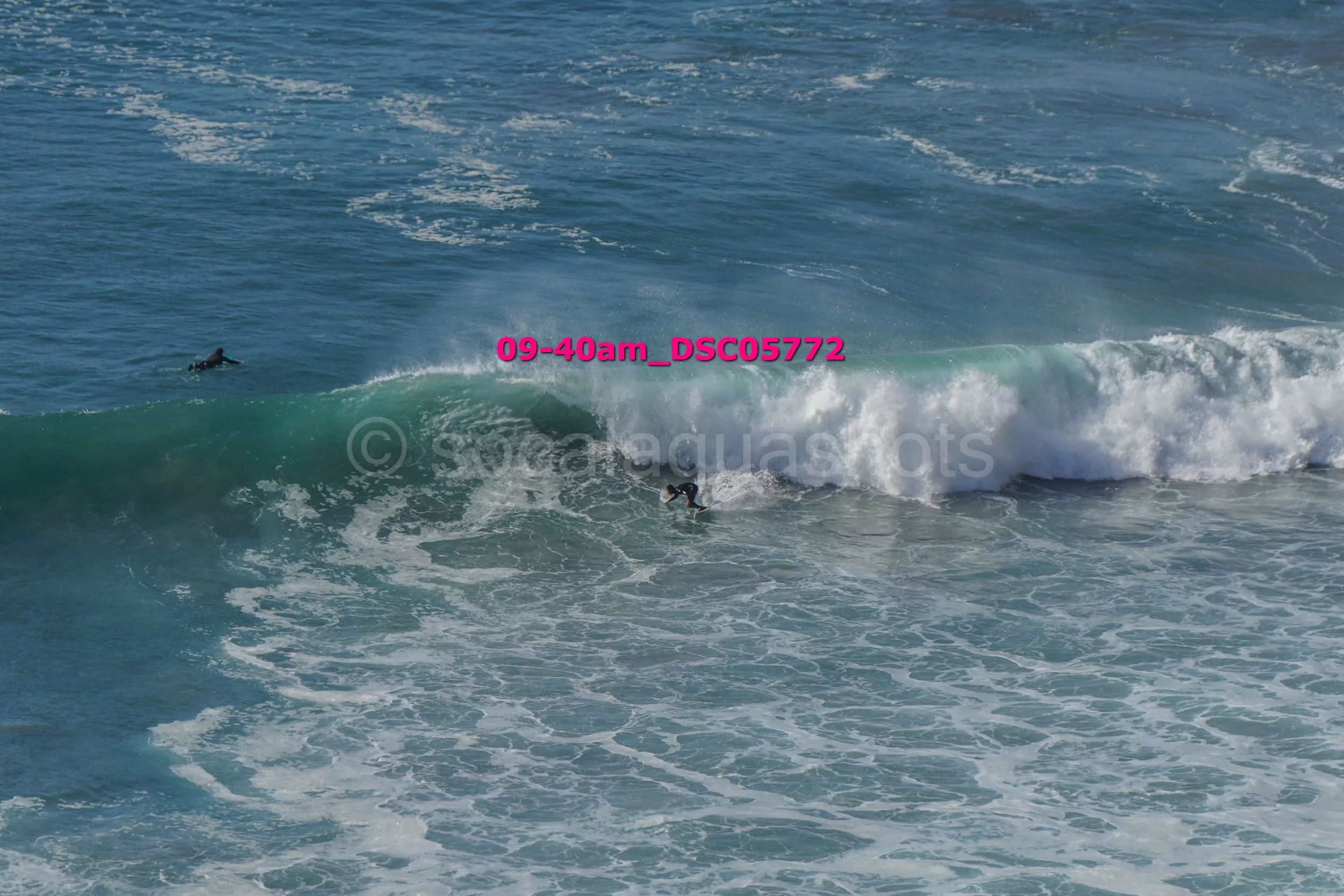 A surfer riding a wave in the ocean with another surfer swimming nearby.