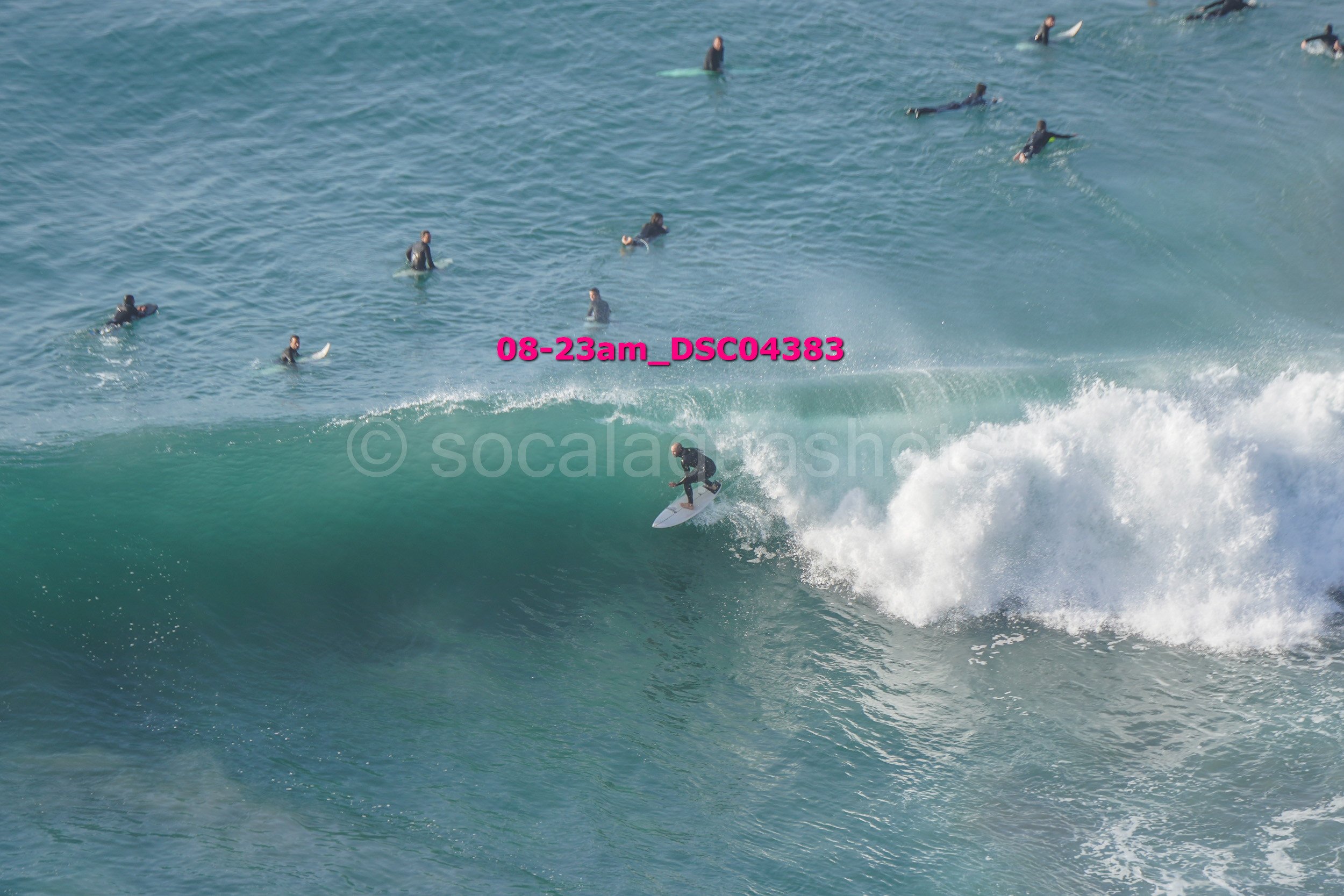 Surfer riding a large wave while multiple surfers float in the water nearby.
