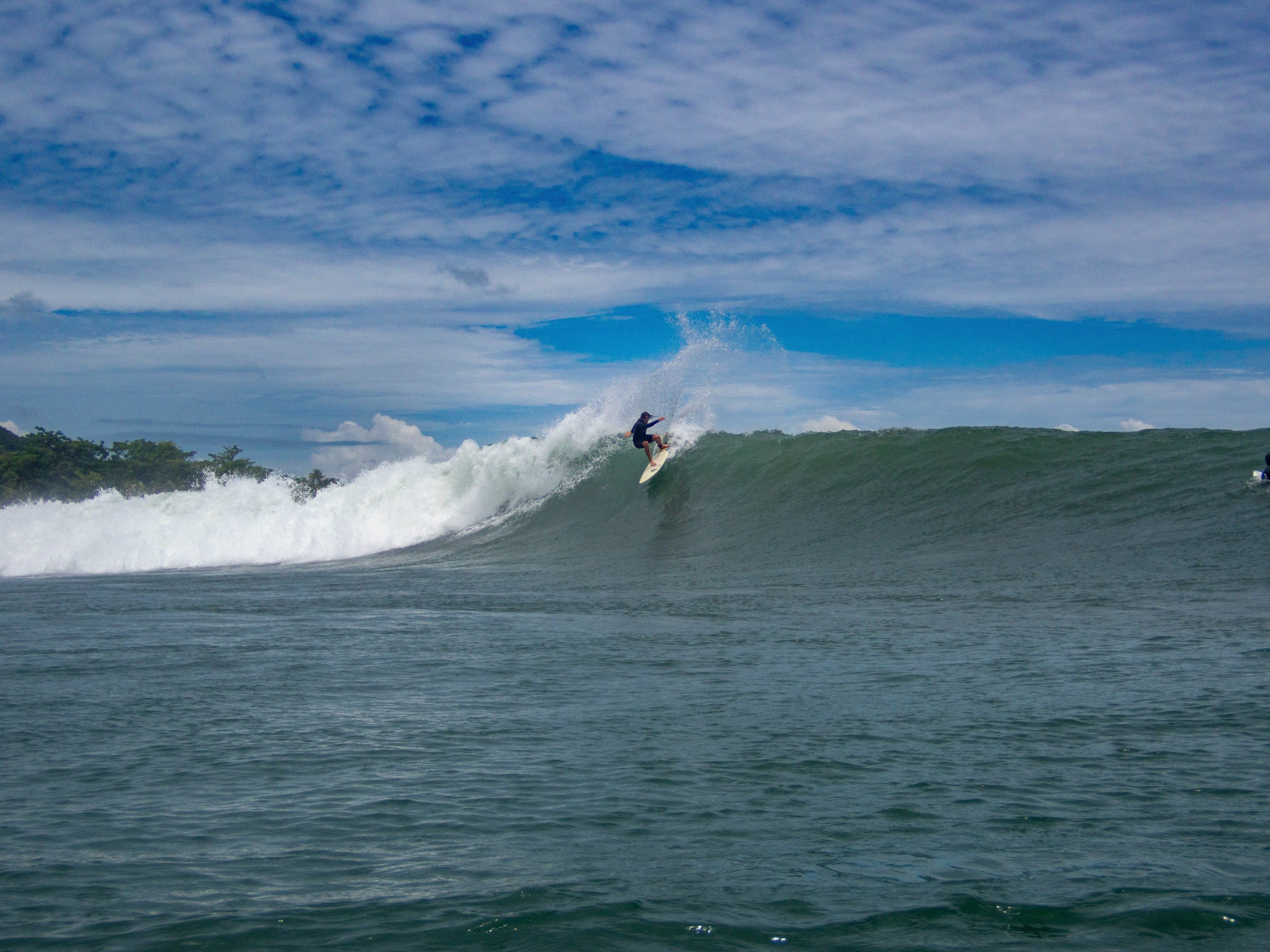 Surfer riding a large wave in the ocean with a blue sky background