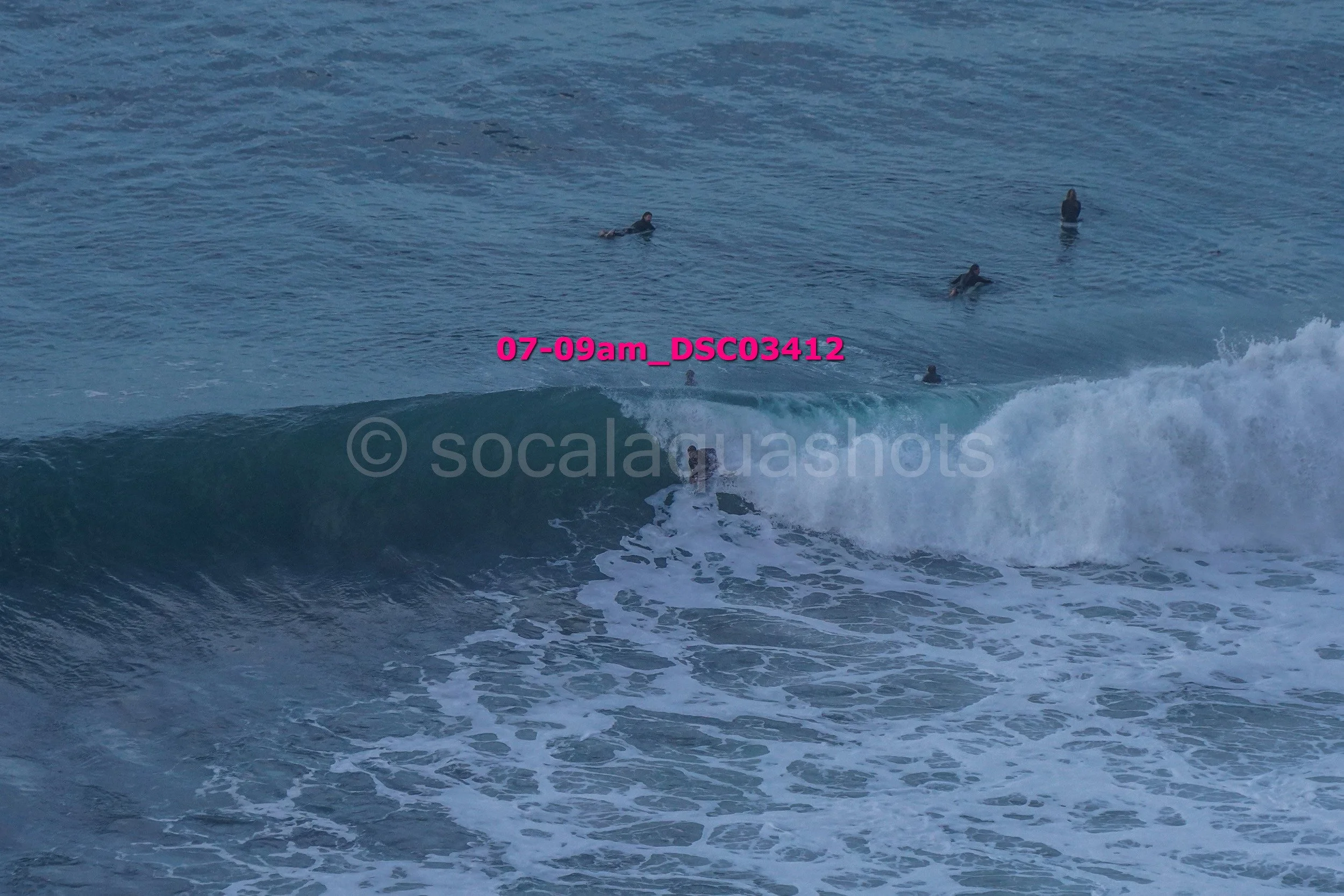 People surfing on a wave in the ocean with some individuals swimming in the water nearby.