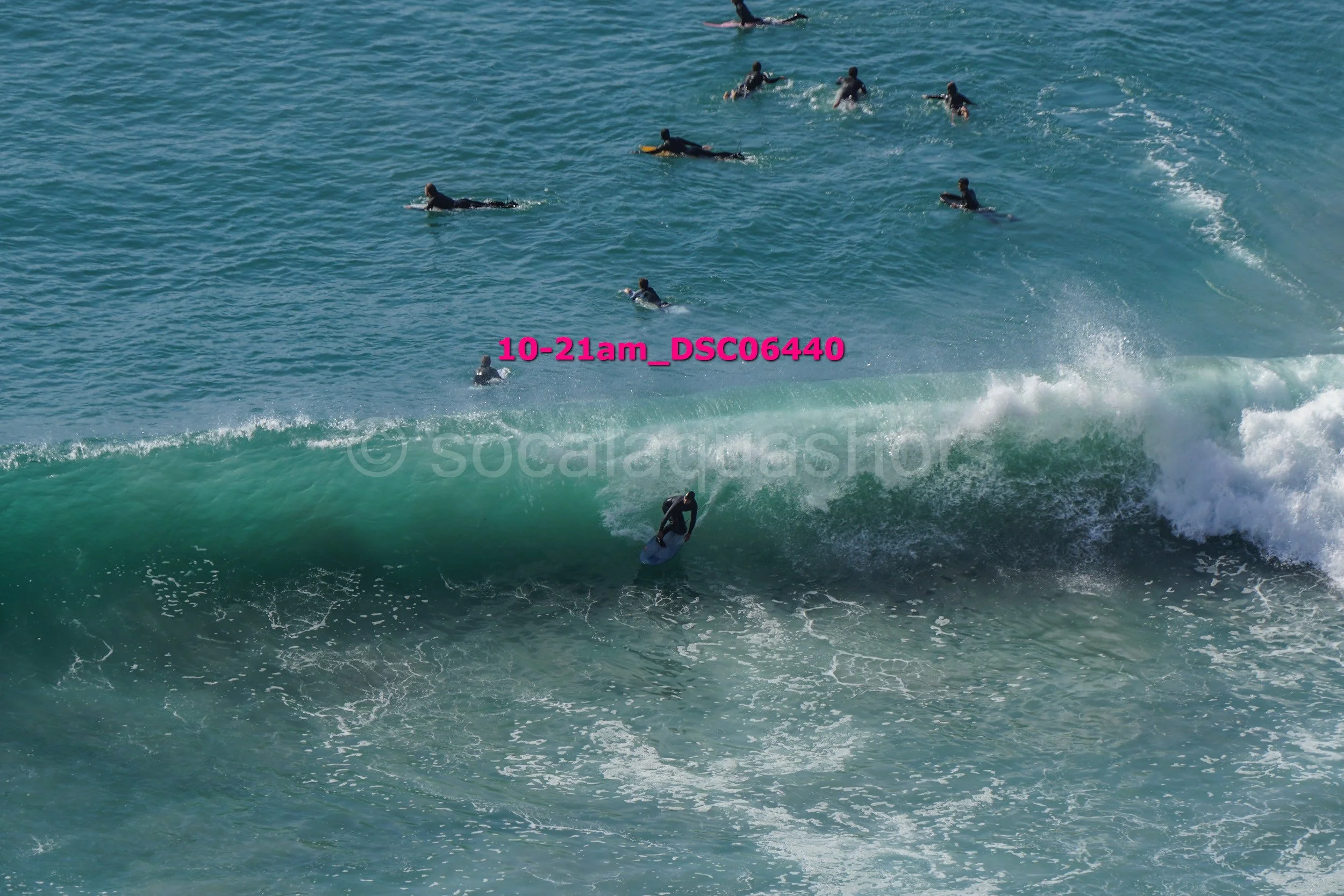 Surfer riding a wave while a group of surfers surf in the distance in the ocean.
