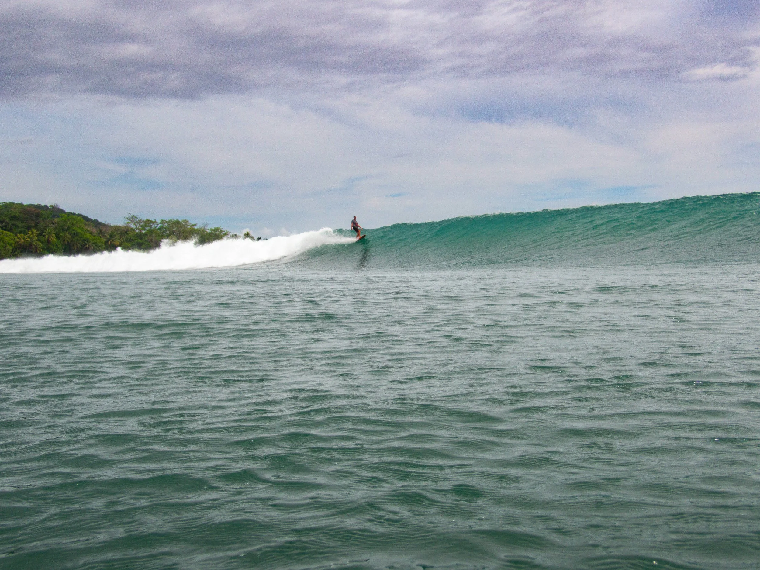 Surfer riding a wave in the ocean with cloudy sky.