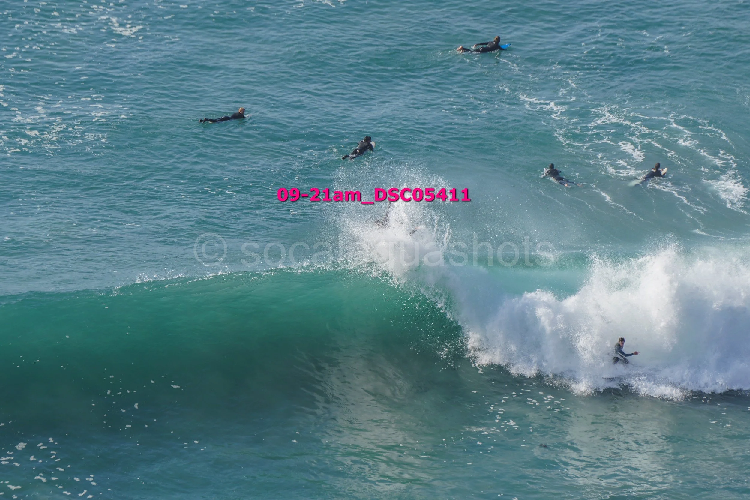 Group of people surfing and swimming in the ocean, with one surfer riding a large wave.