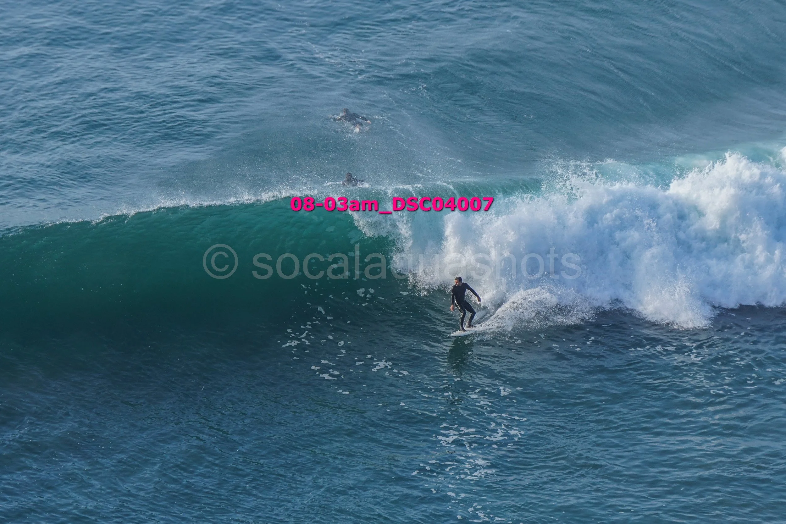 A person surfing on a wave in the ocean with a few other surfers in the background.