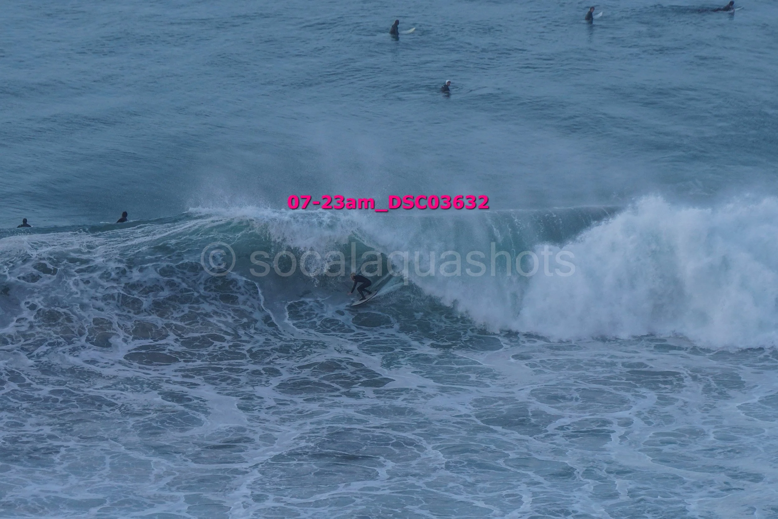 A surfer riding a wave in the ocean with several people swimming in the water in the background.