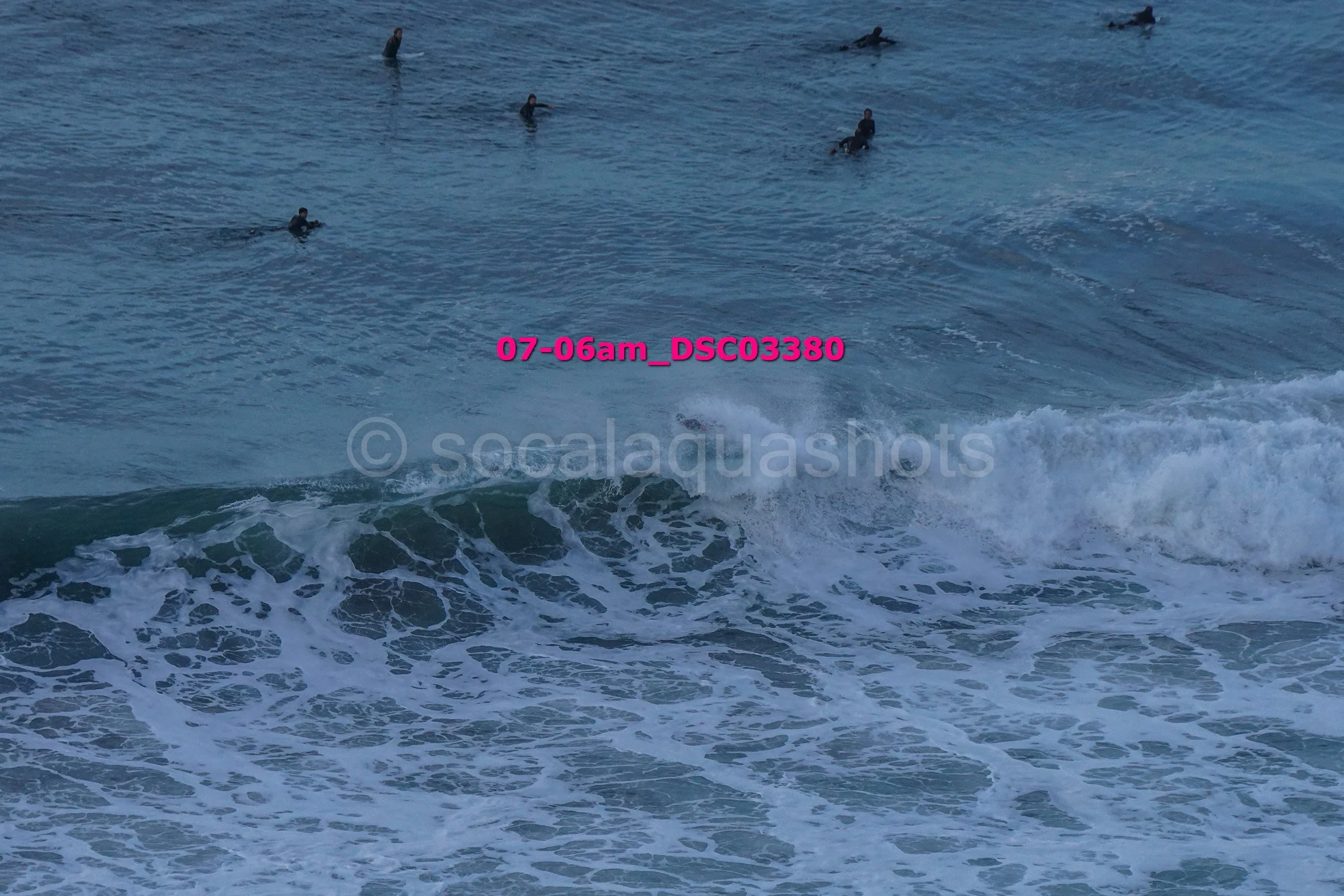 Group of people swimming in the ocean, some riding small waves, sea water and surf visible.