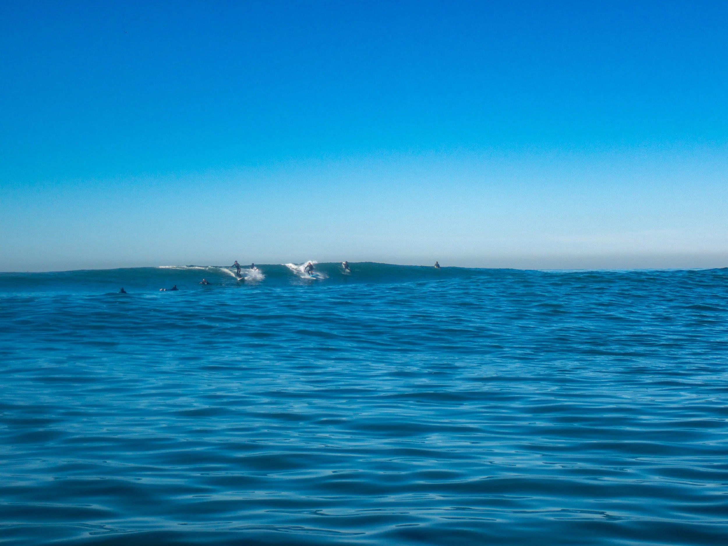 Surfers riding waves in the ocean under a clear blue sky.