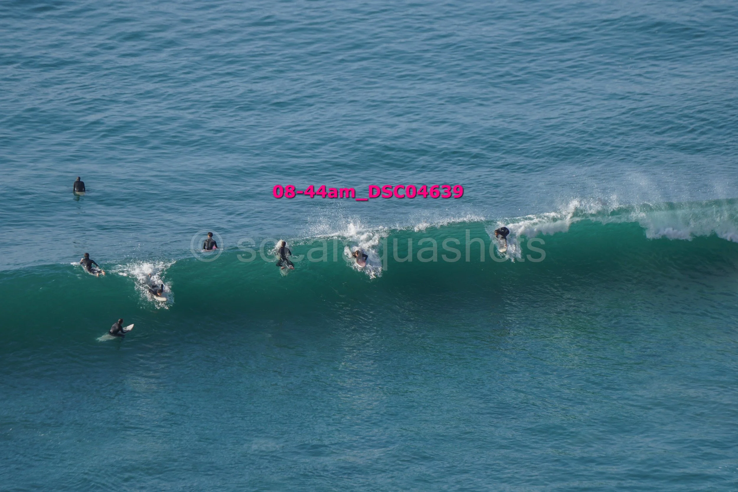 Multiple surfers riding and waiting on a large ocean wave during daytime.