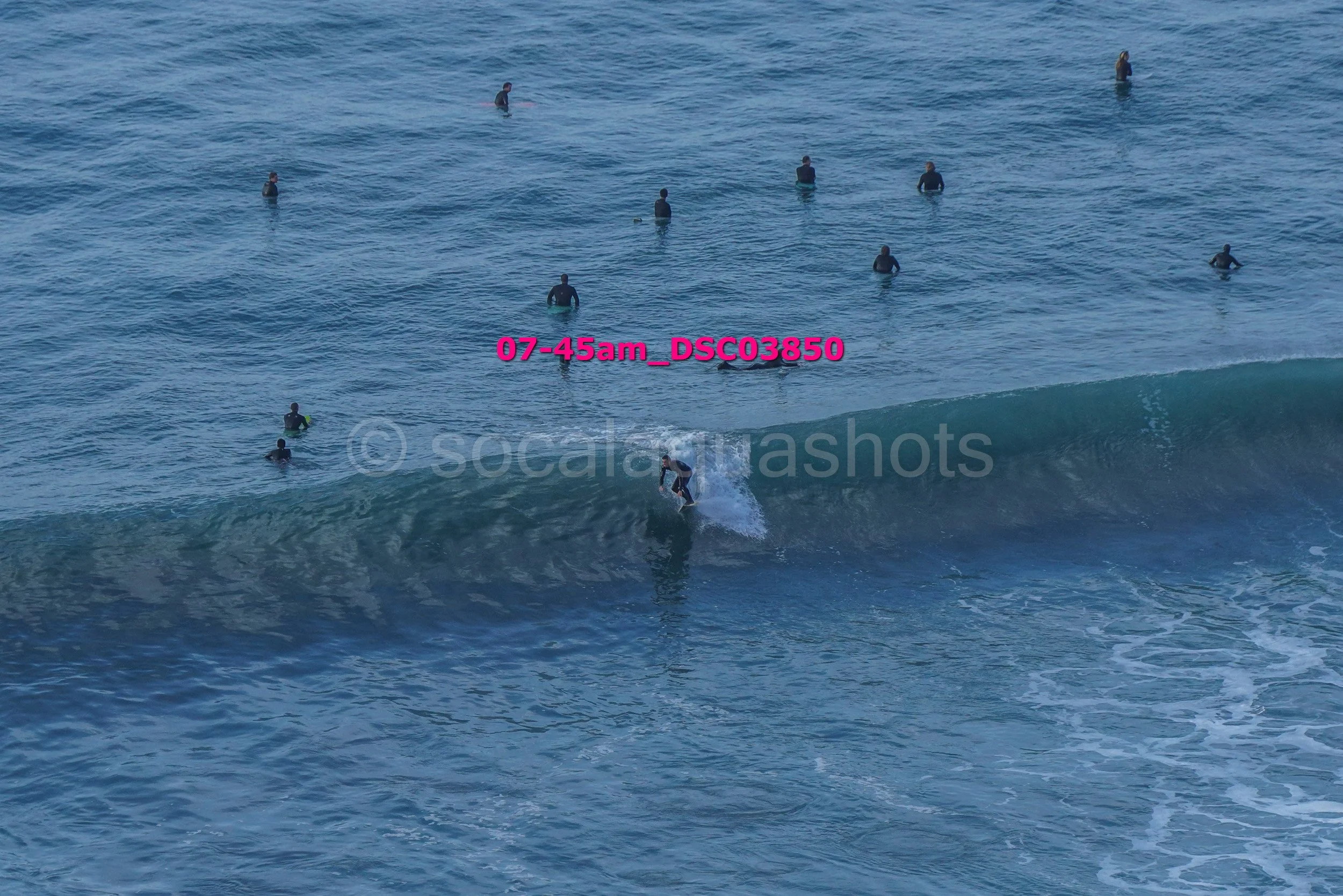 A person surfing on a wave with multiple people in the water nearby in the ocean at sunrise.