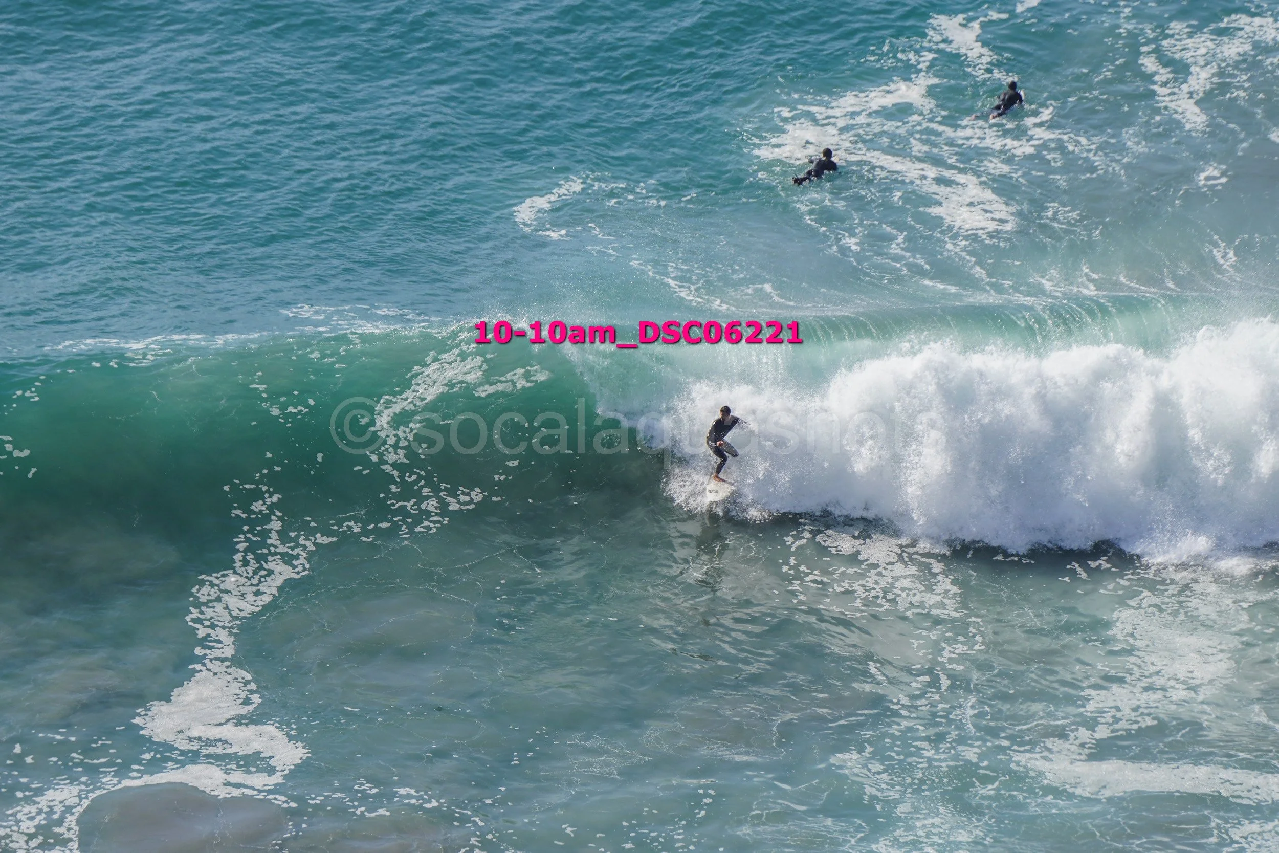 Surfer riding a wave with three other surfers in the background in the ocean.