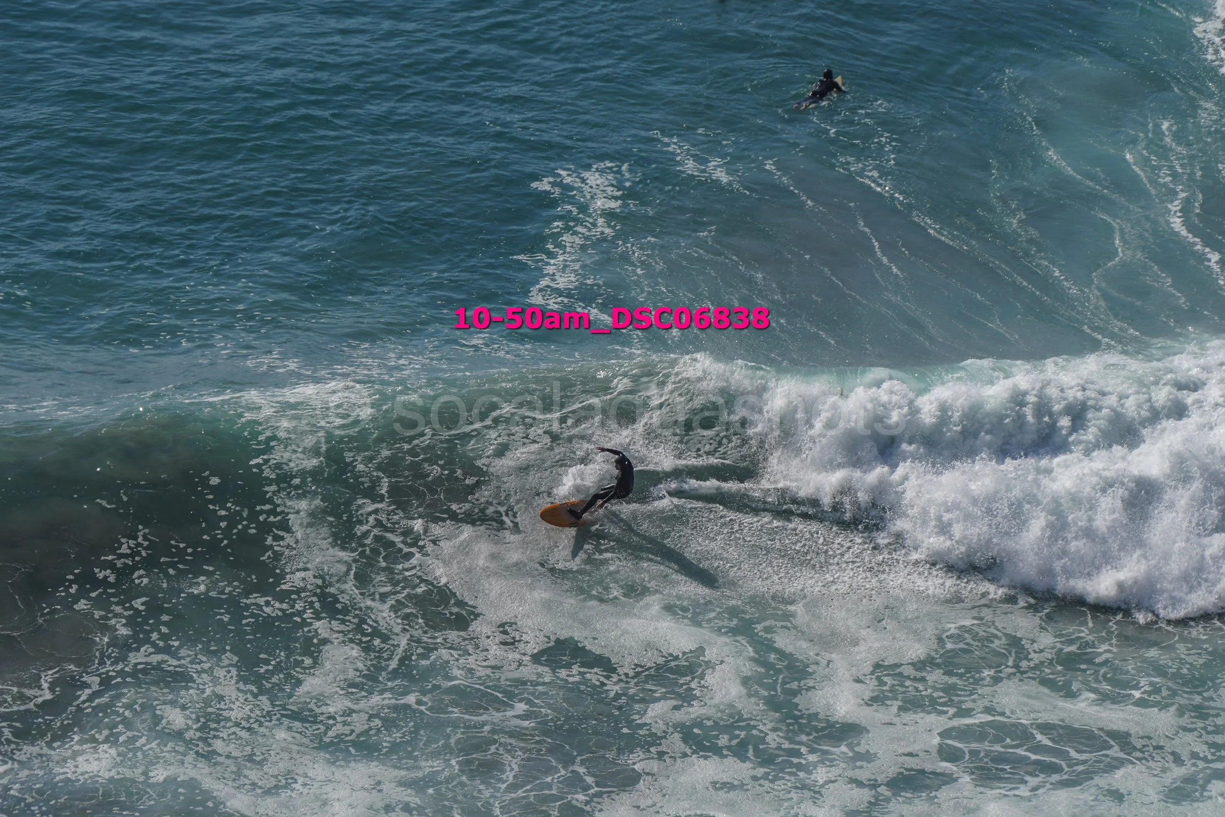 A person surfing on a wave in the ocean with another surfer in the background.