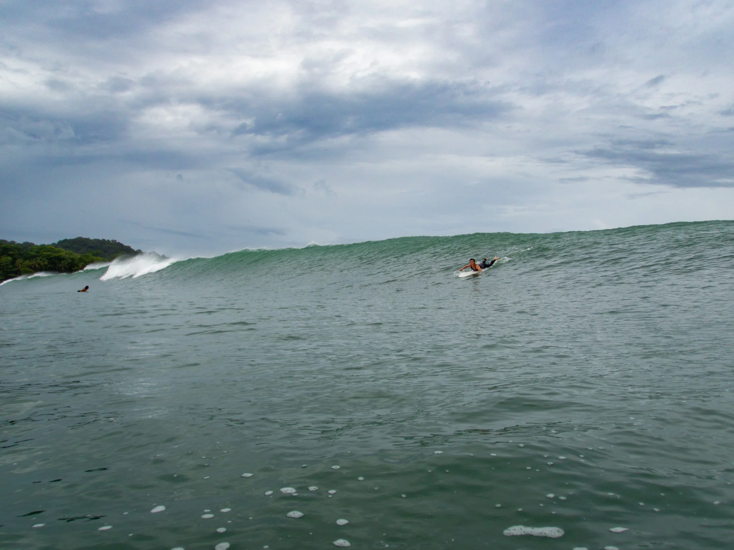 Surfer paddling on a large ocean wave under a cloudy sky