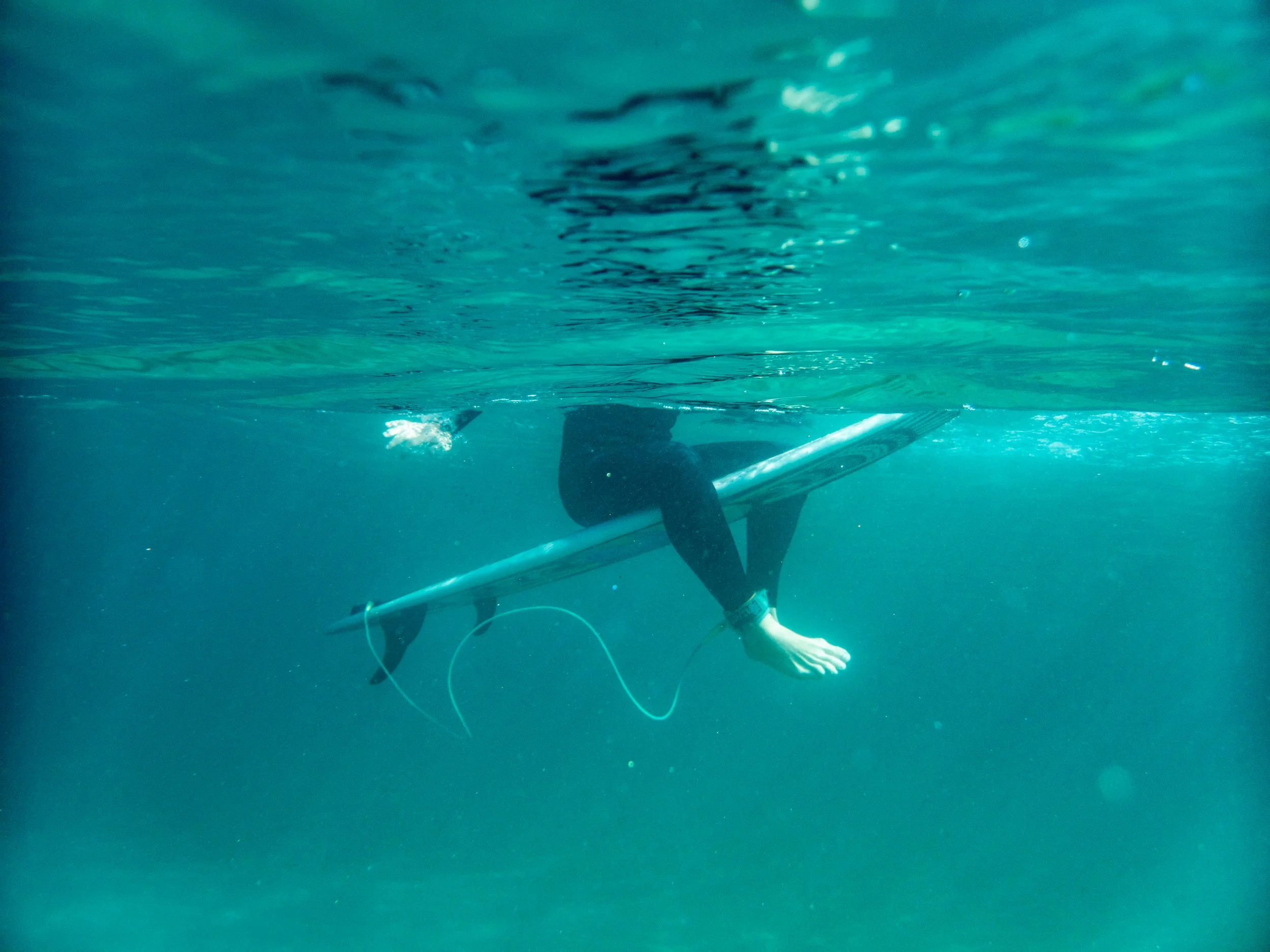 Person in black wetsuit holding a surfboard while surfing underwater.