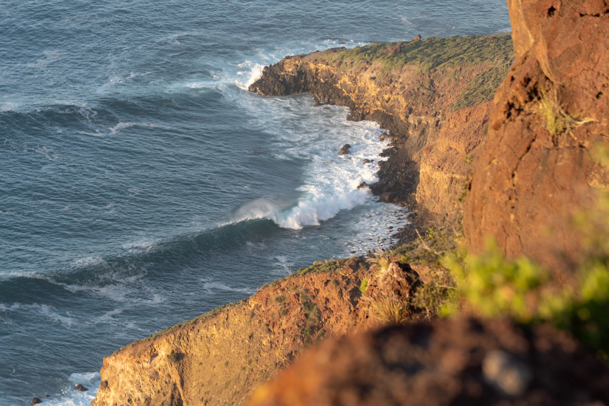 Cliffside with ocean waves crashing against rocks during sunset