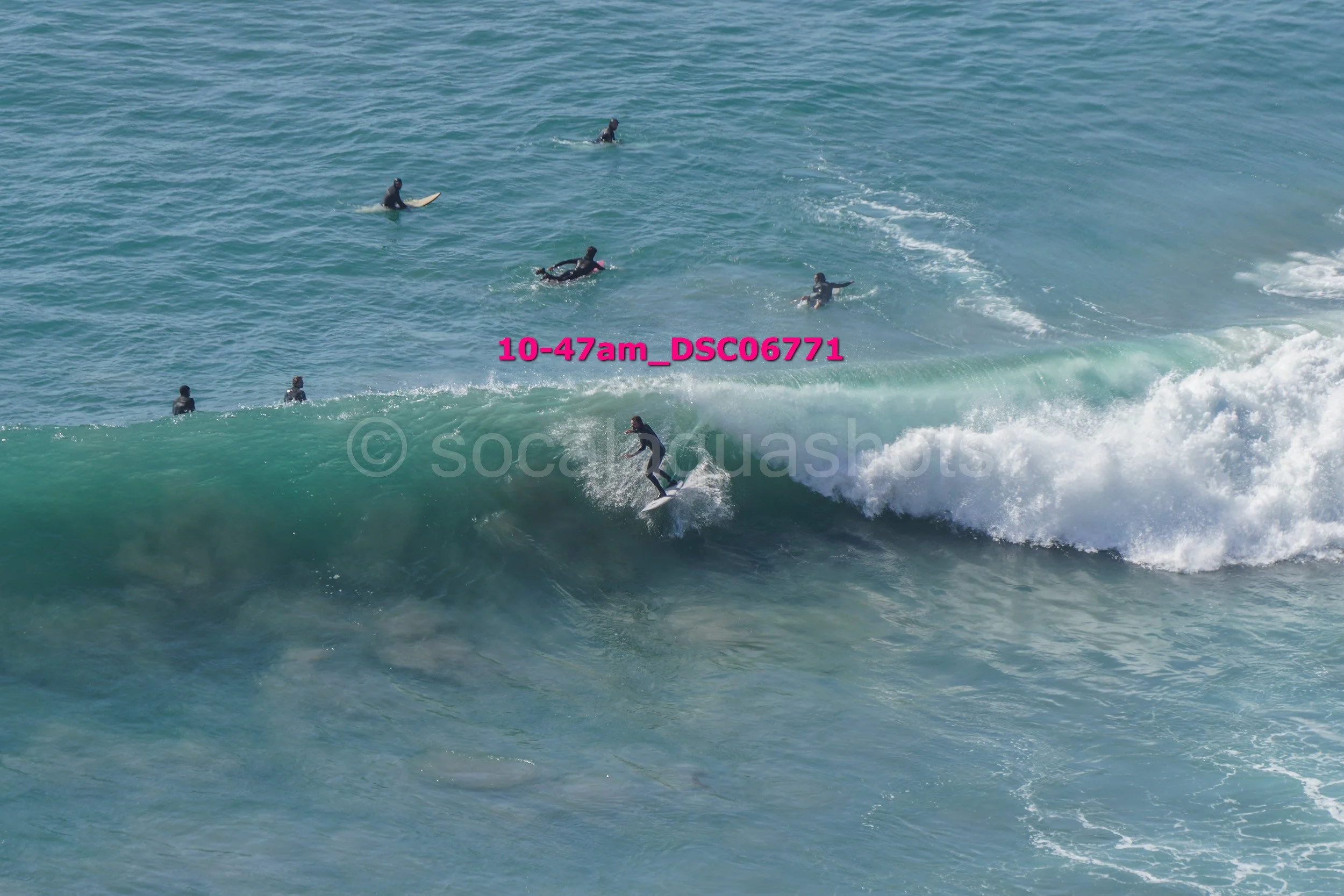 A person surfing a large wave with several other surfers waiting nearby in the water.