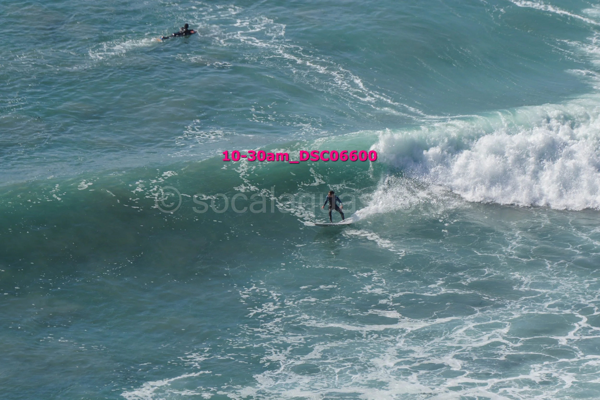 A person surfing on a wave in the ocean, with another person swimming in the water nearby.