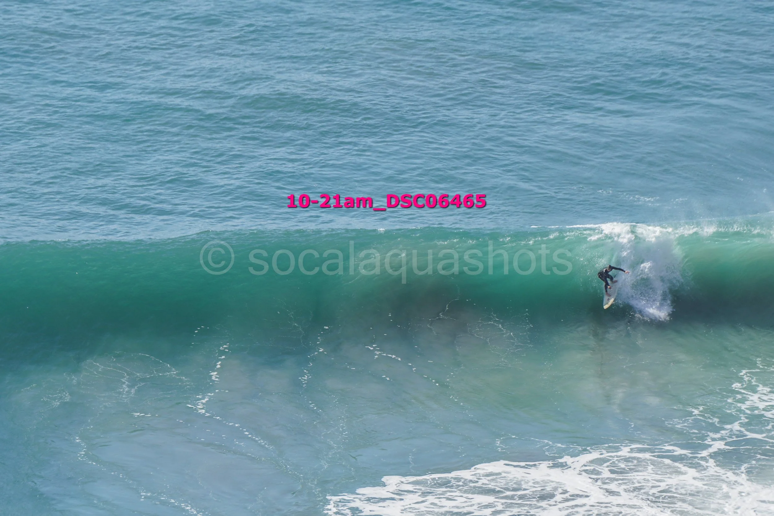A surfer in a black wetsuit riding a large wave in the ocean.