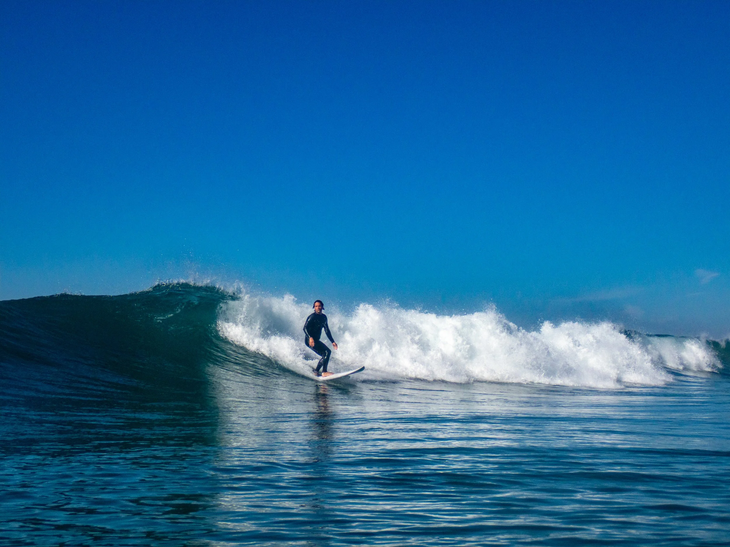 A person surfing on a wave in the ocean under a clear blue sky.
