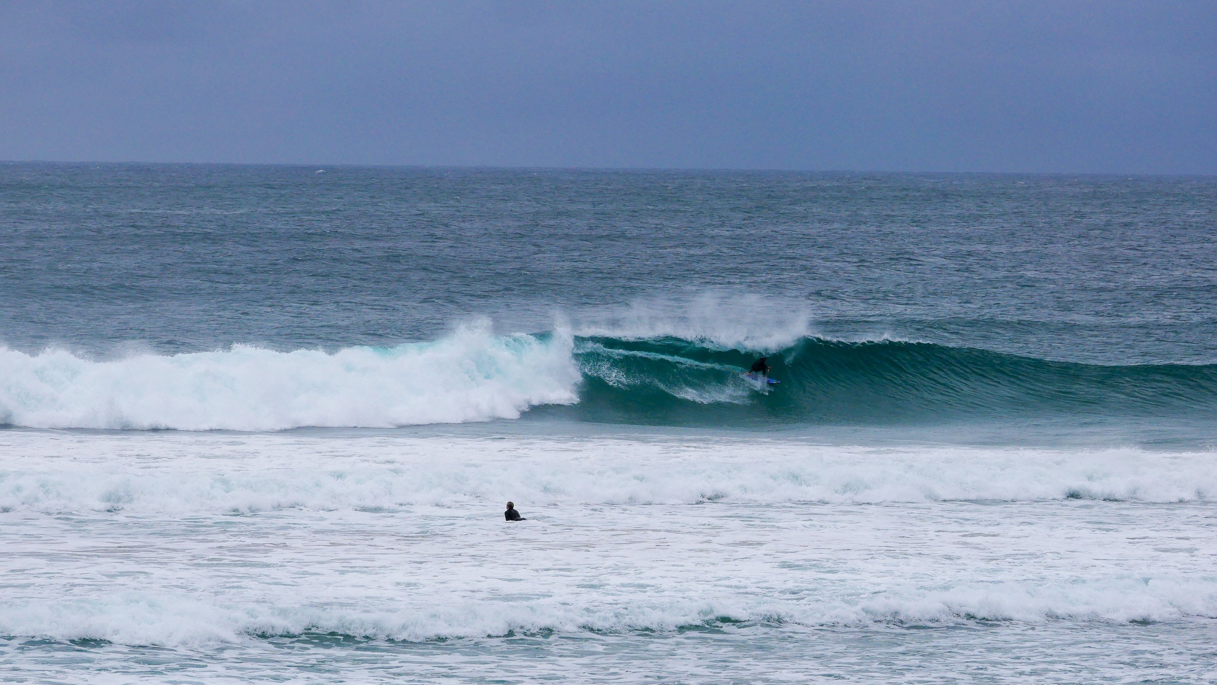Surfer riding a large wave in the ocean with another person in the water nearby.