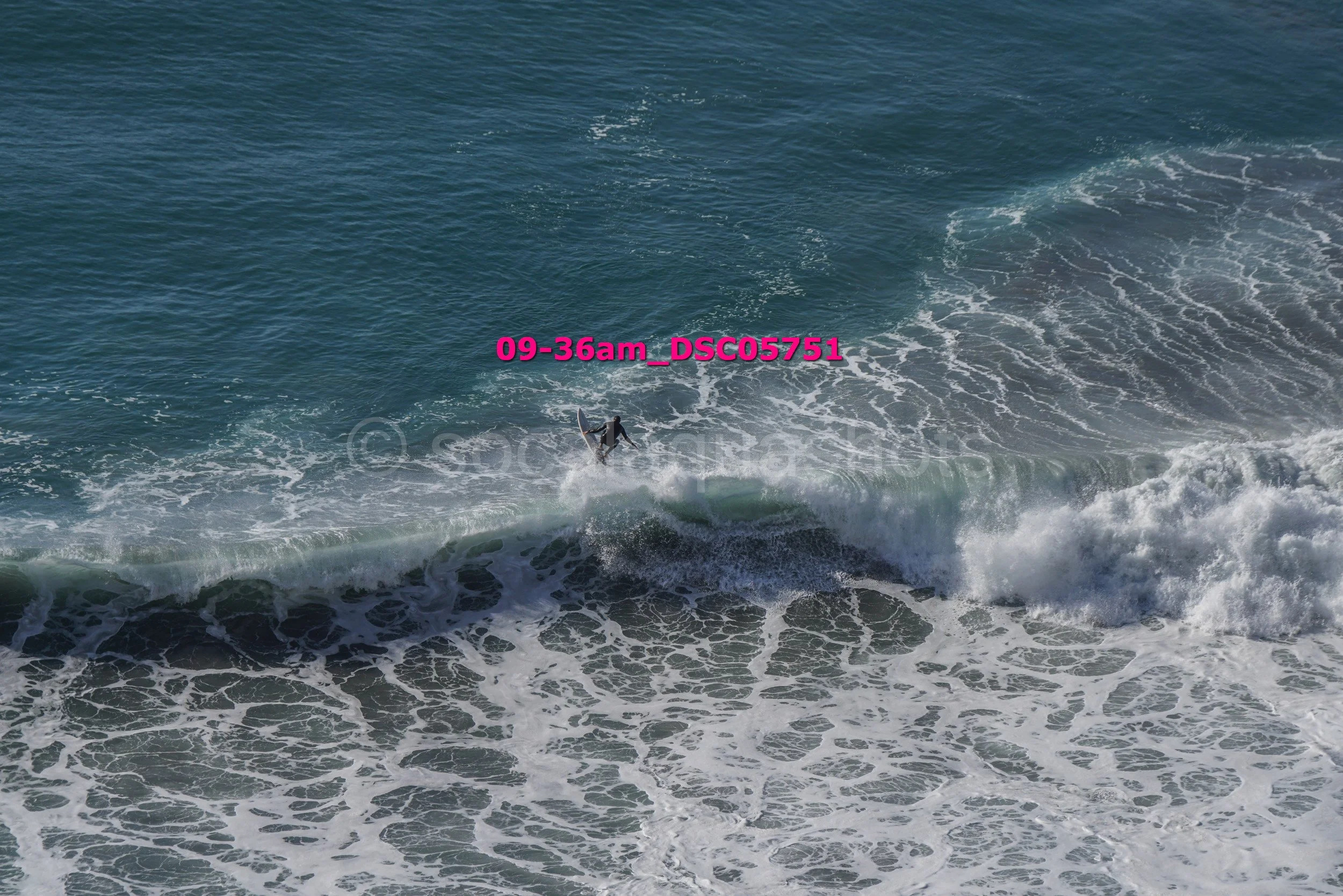 A person surfing on a wave in the ocean, viewed from above.