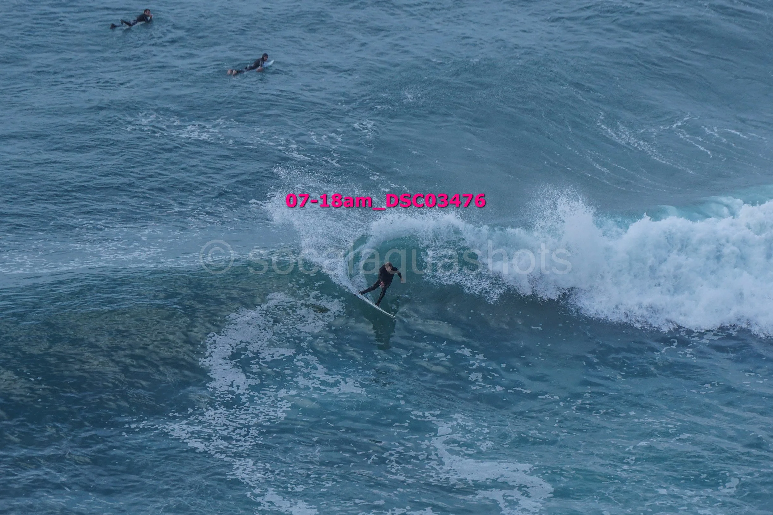 A person surfing on a wave in the ocean with three other surfers in the background.