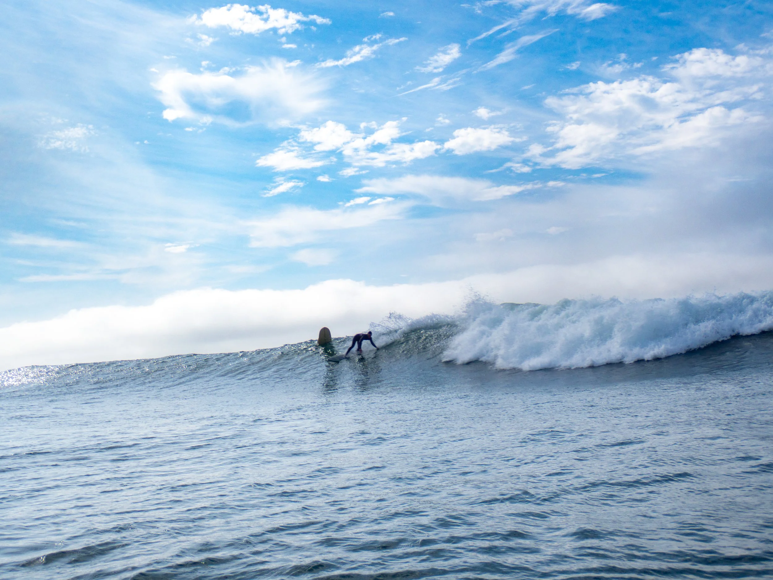 A surfer riding a wave in the ocean under a partly cloudy sky.
