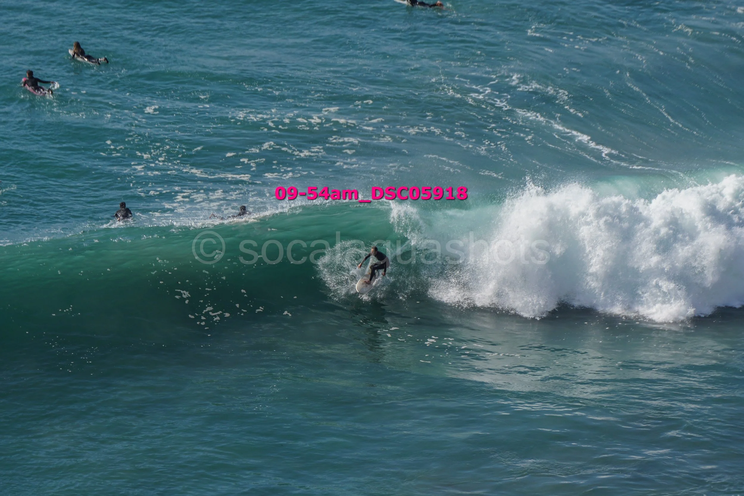 Surfer riding a wave with several people in the water in the background.
