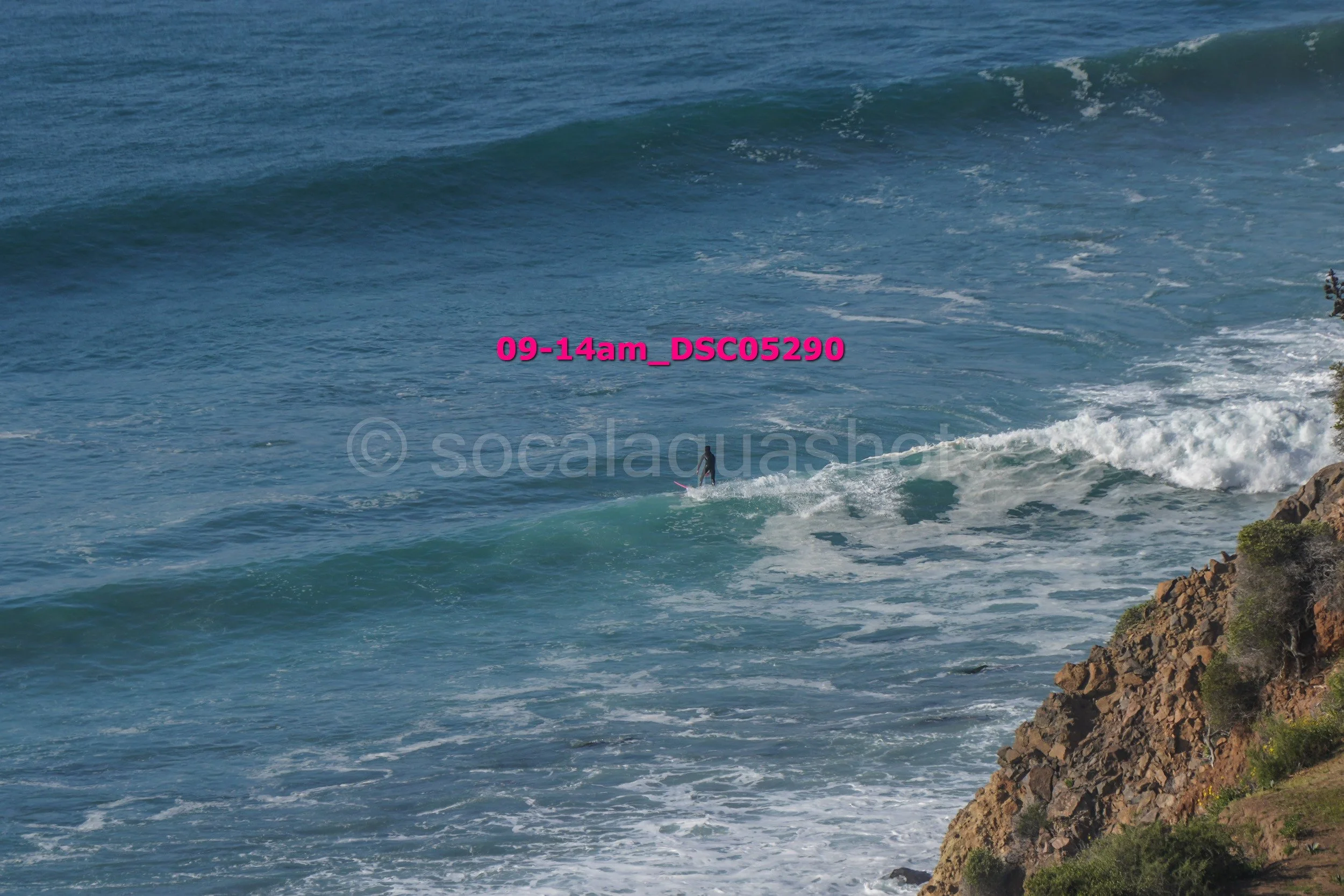 A surfer riding a wave near a rocky coastline.