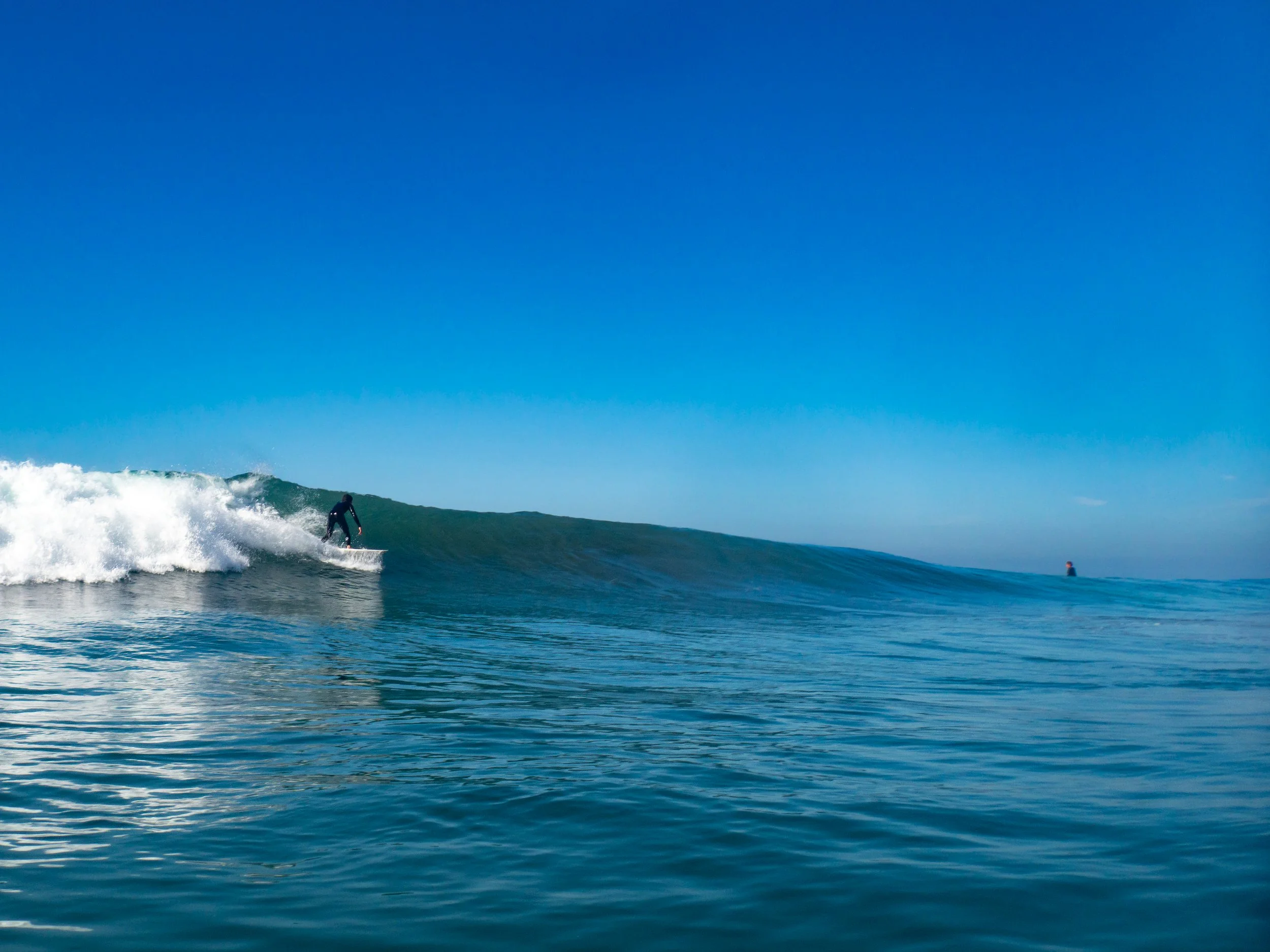 A person surfing on a wave in the ocean under a clear blue sky.