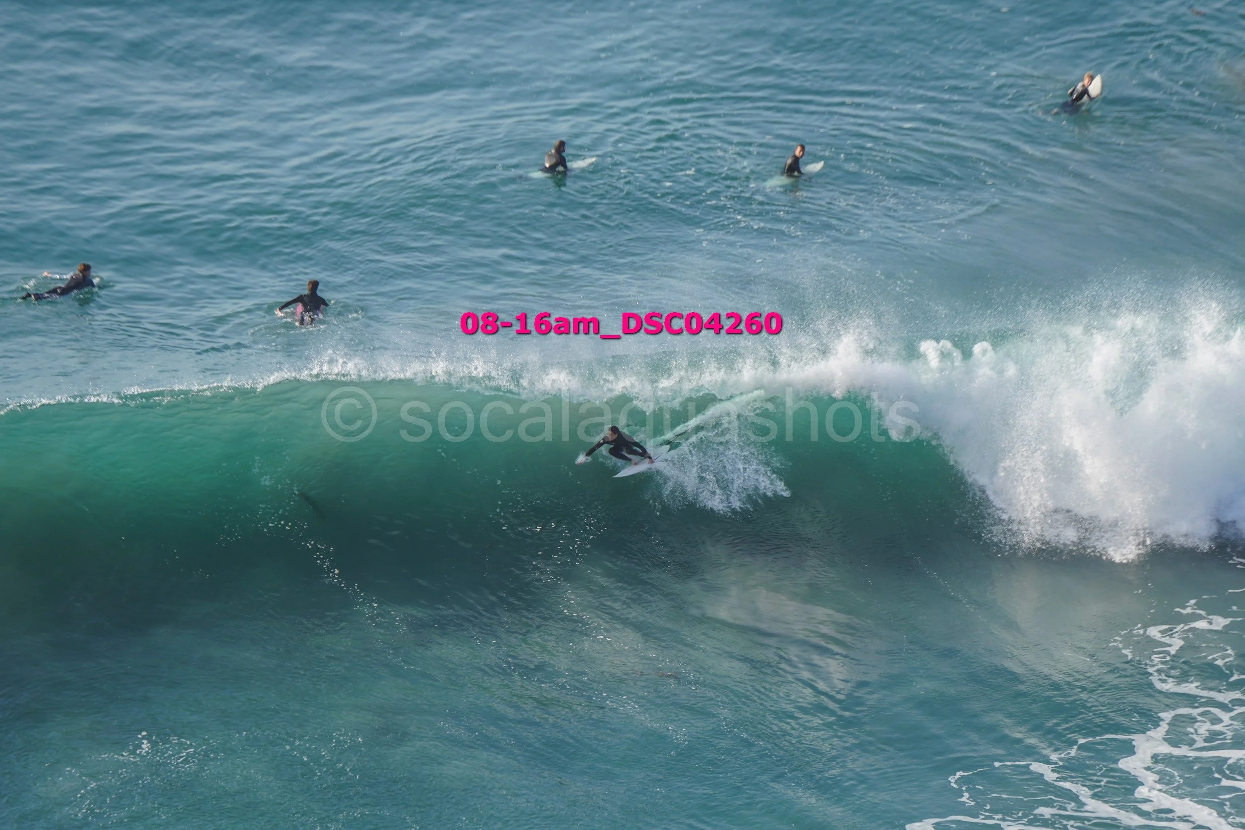 A group of surfers in wetsuits riding and waiting on a large wave in the ocean.