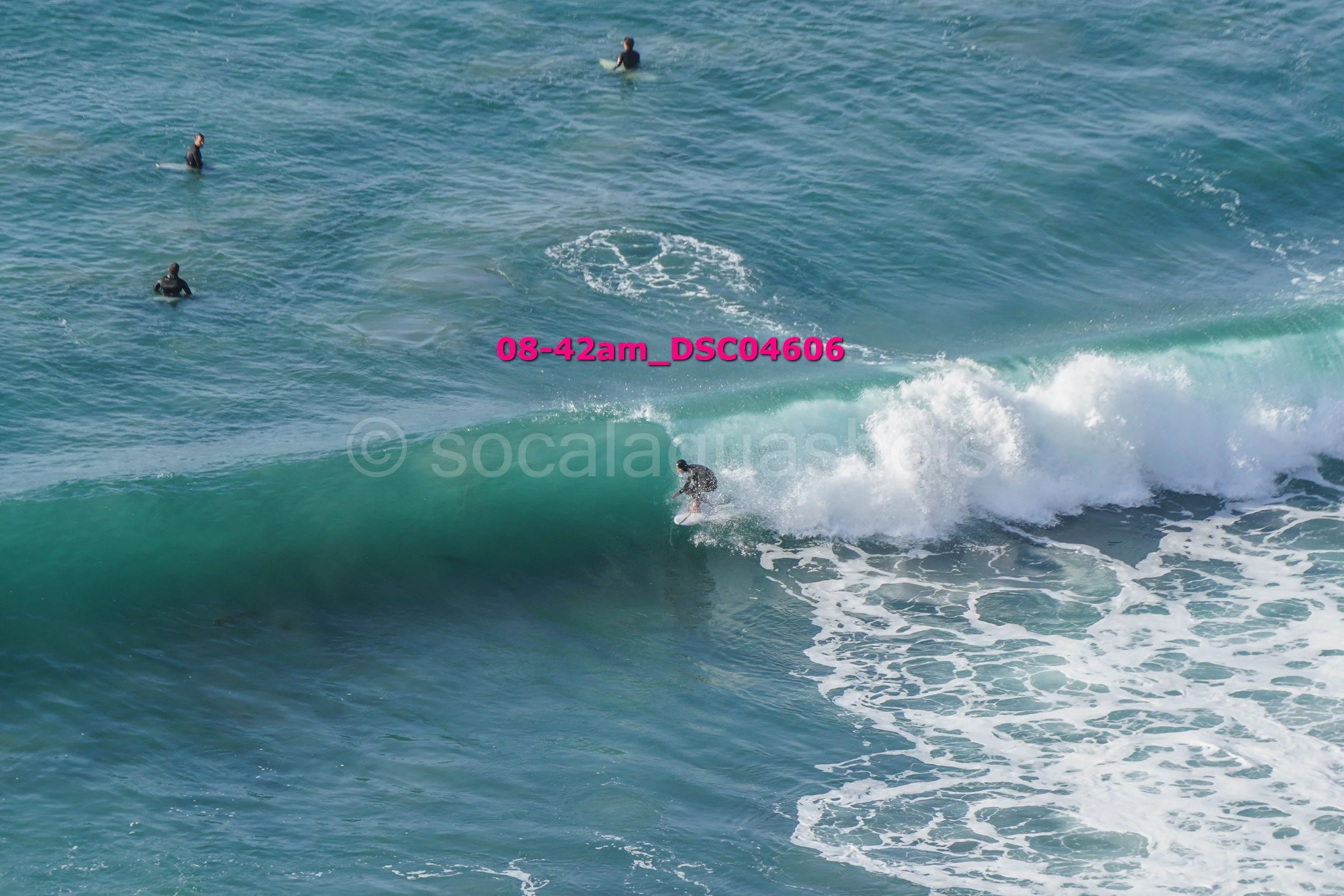 Surfer riding a wave in the ocean with three other surfers in the background.
