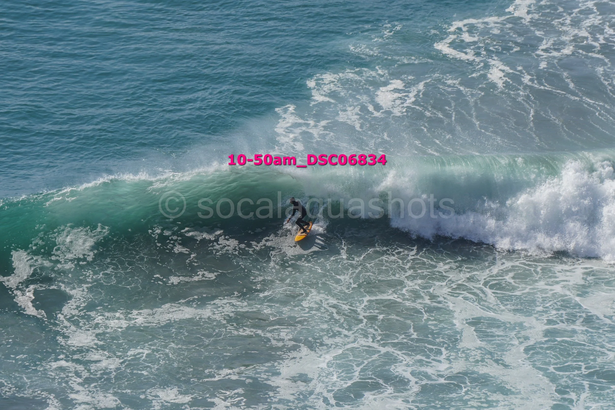 A person surfing on a large ocean wave with a clear blue sky in the background.