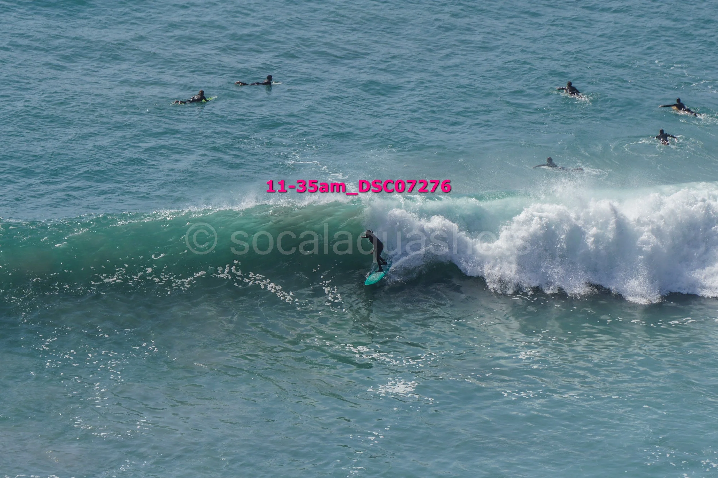 A person surfing on a wave with several other surfers in the water nearby.