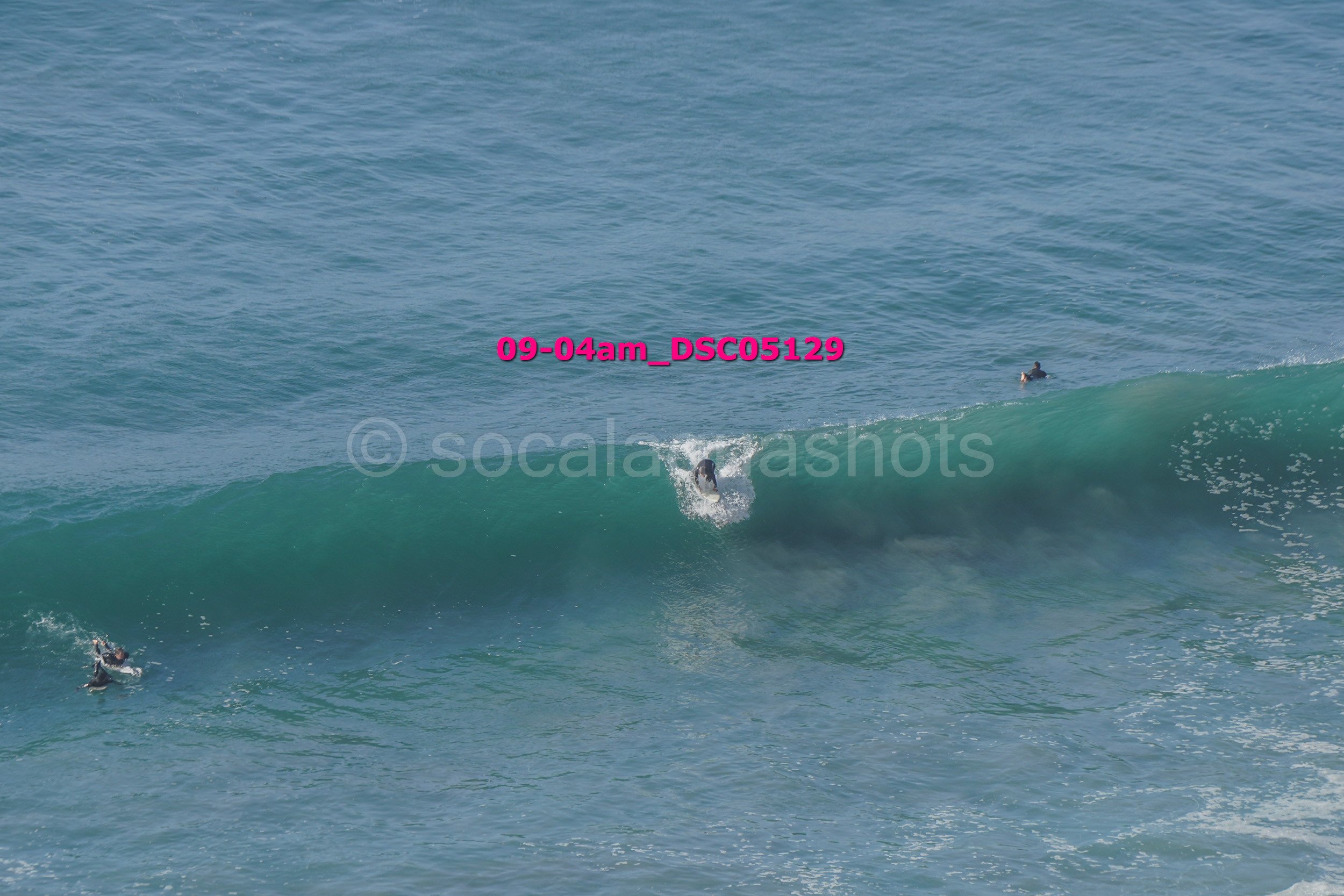 Surfers riding and paddling on ocean waves during daytime.